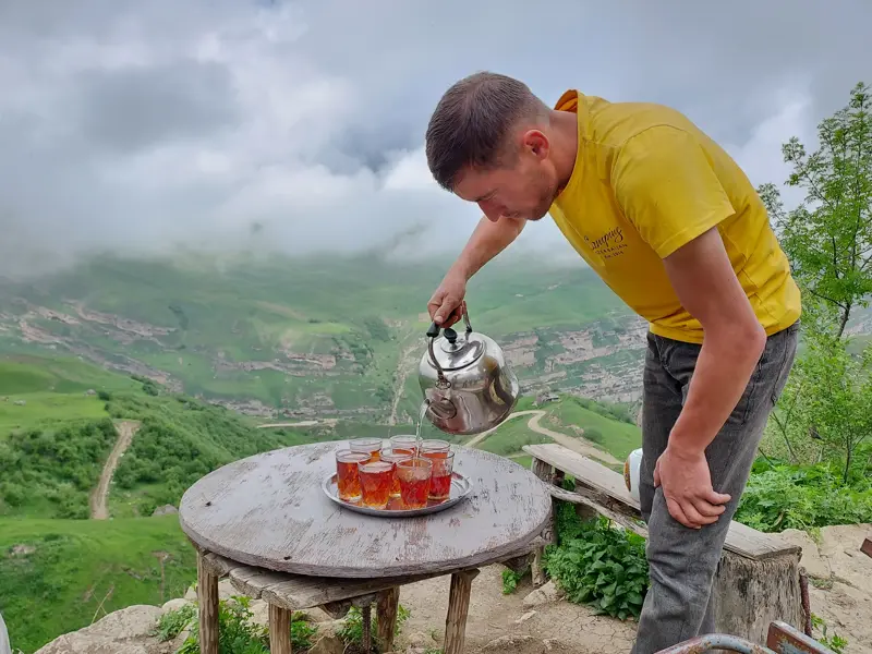 Teepause während einer Trekkingtour: Ein Mann schenkt Tee ein vor der grünen Berglandschaft des Großen Kaukasus.