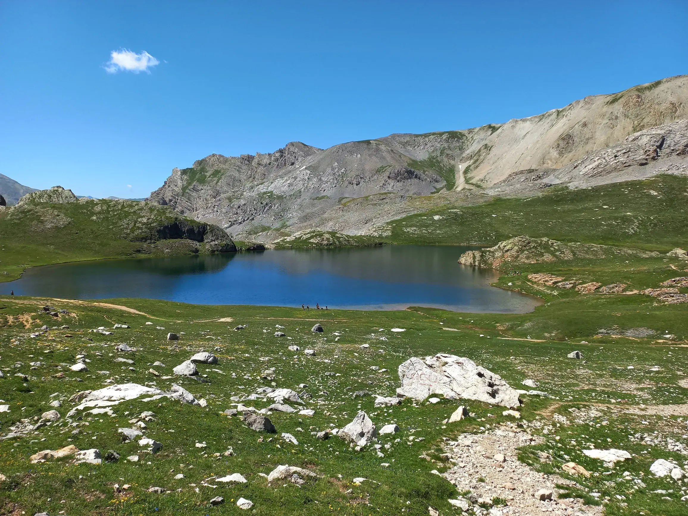 Klarer Bergsee Lago Apzoi im Maira-Tal, umgeben von grünen Almwiesen und schroffen Felsmassiven der Alpen im Piemont.