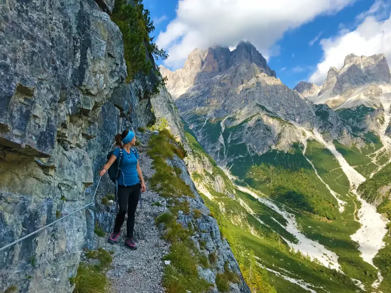 Wanderin auf einem schmalen, seilgesicherten Felsensteig blickt auf die schroffen Gipfel der Brenta-Dolomiten im Trentino.