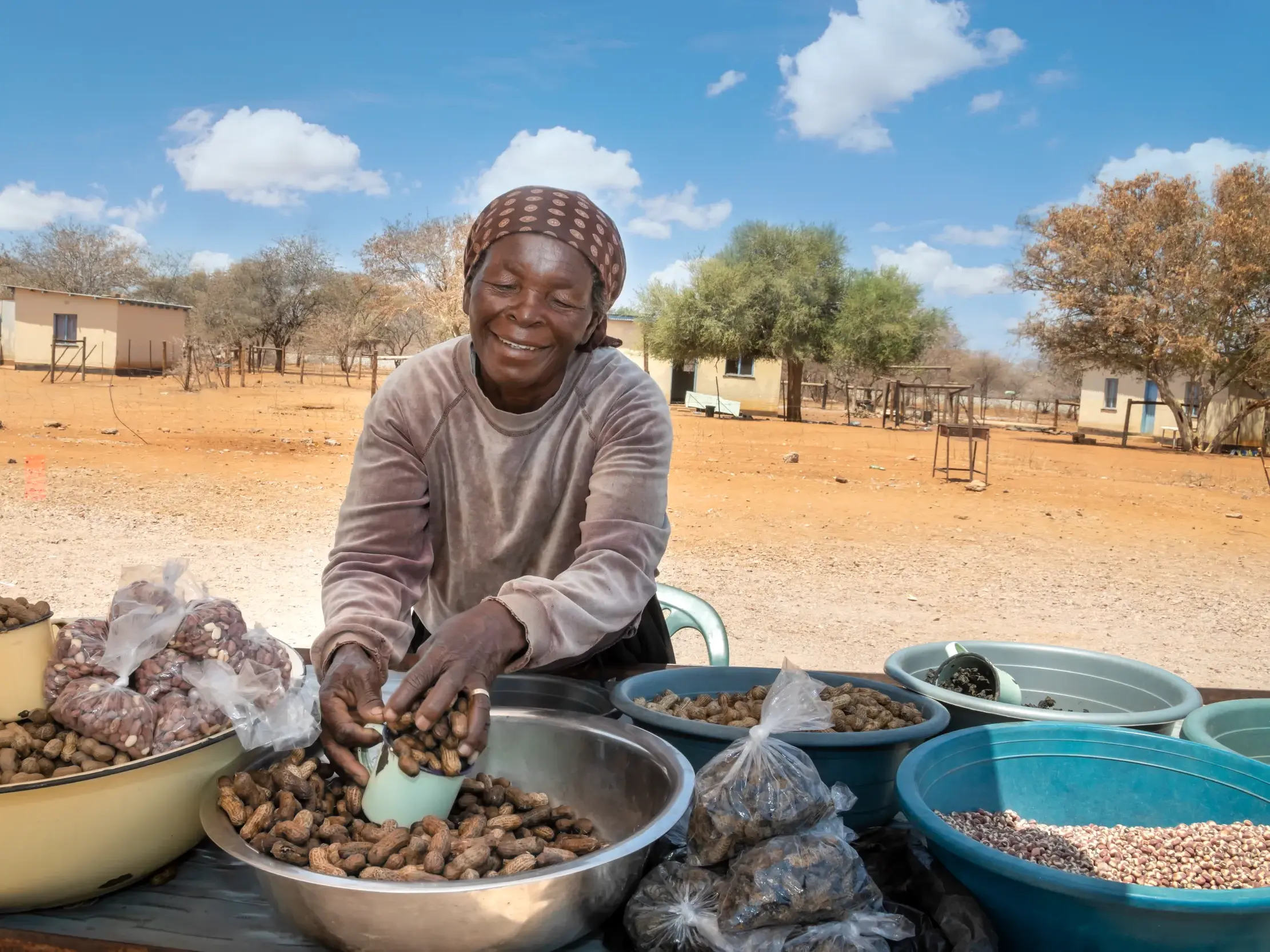 Eine lächelnde Verkäuferin füllt an ihrem Marktstand in einem Dorf in Botswana Erdnüsse aus einer großen Schale ab.