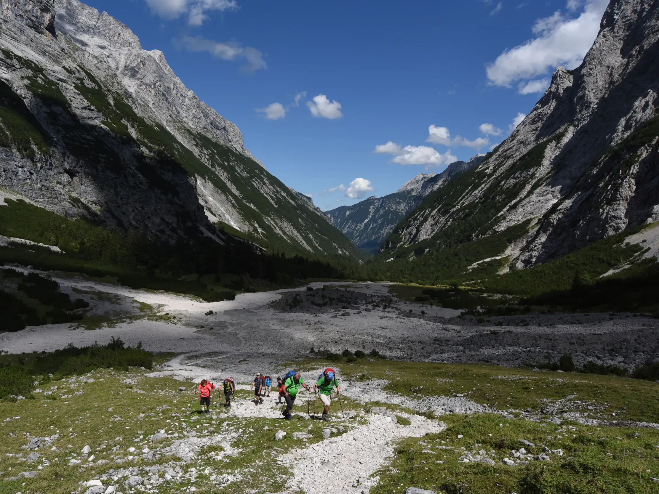 Eine Hauser-Trekkinggruppe wandert auf einem Schotterpfad durch das weite, sonnige Reintal in Richtung Zugspitze.