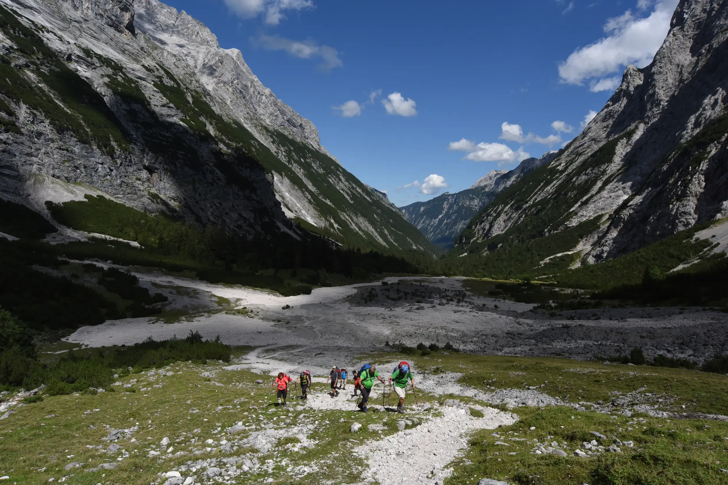 Eine Hauser-Trekkinggruppe wandert auf einem Schotterpfad durch das weite, sonnige Reintal in Richtung Zugspitze.