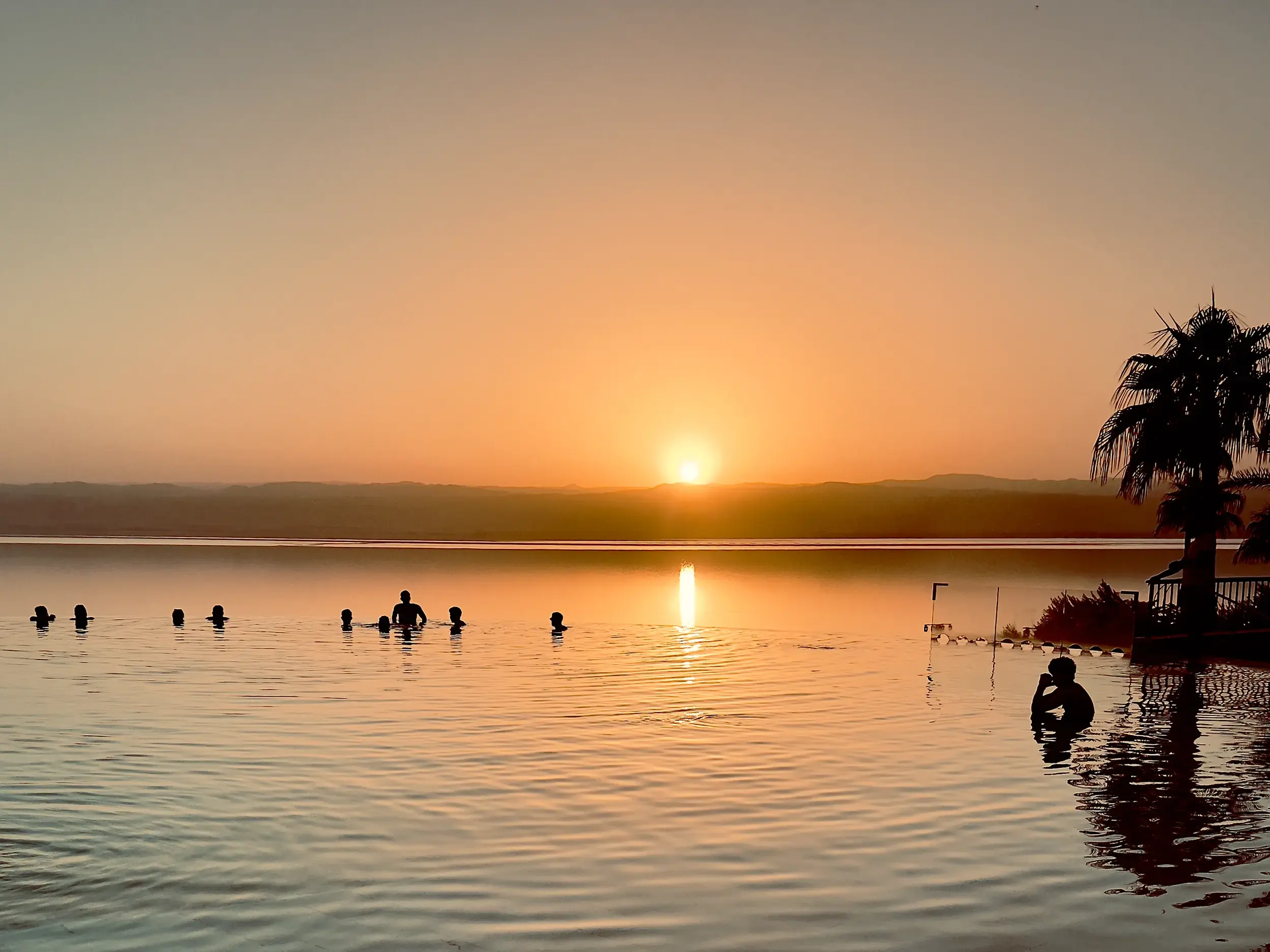 Eine Gruppe junger Leute lässt sich beim Sonnenuntergang entspannt im Salzwasser des Toten Meeres in Jordanien treiben.