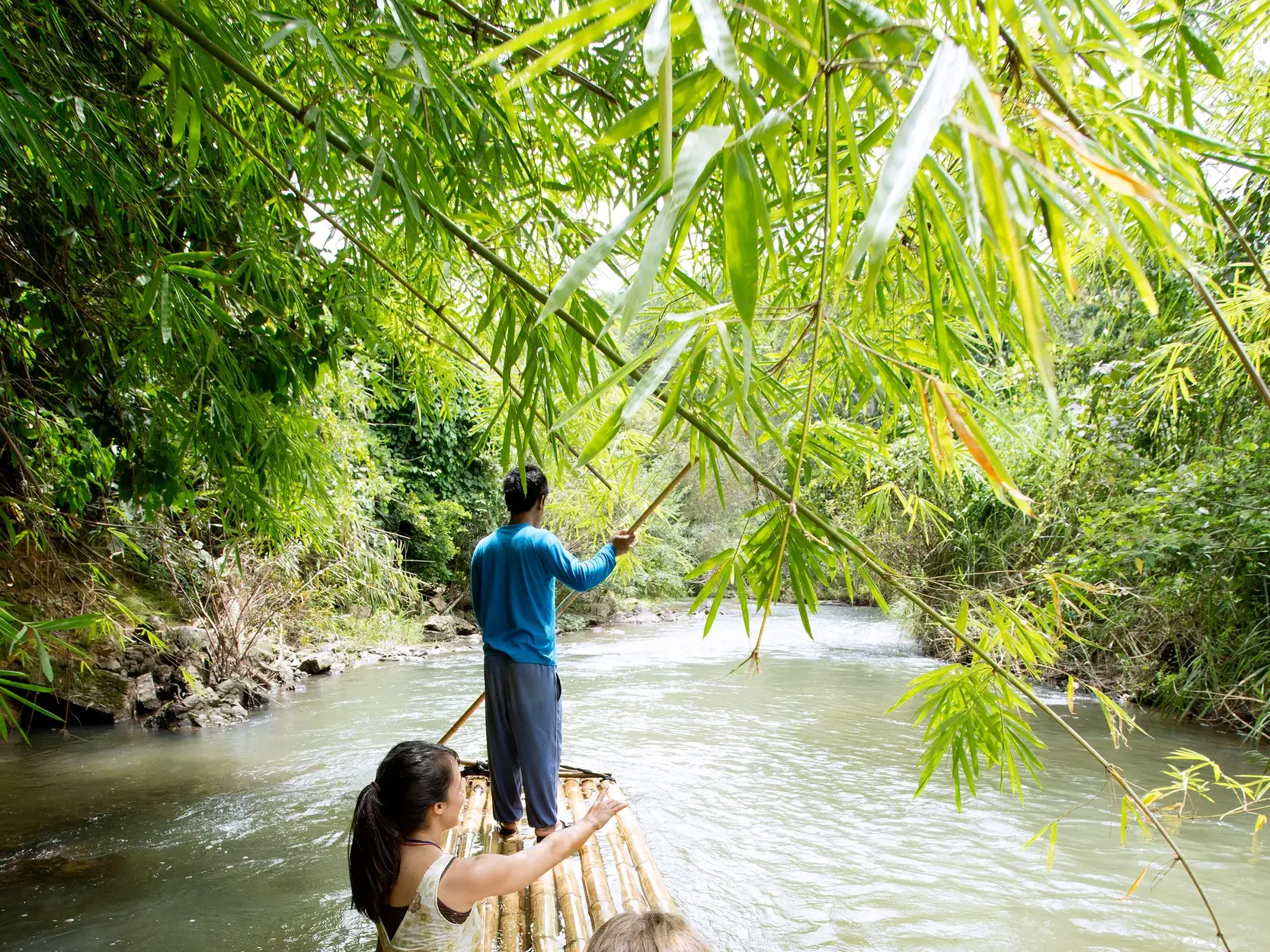 Junge Leute auf einer abenteuerlichen Bambusfloßfahrt auf dem River Kwai während einer geführten Rundreise durch Thailand.
