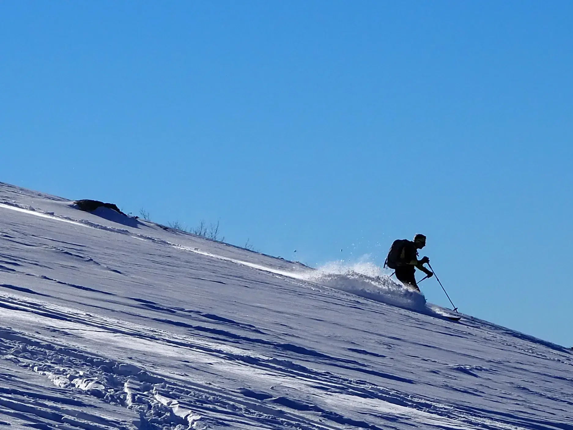 Ein Skitourengeher zieht bei strahlendem Sonnenschein Spuren in den unberührten Pulverschnee an einem Berghang im Balkan.