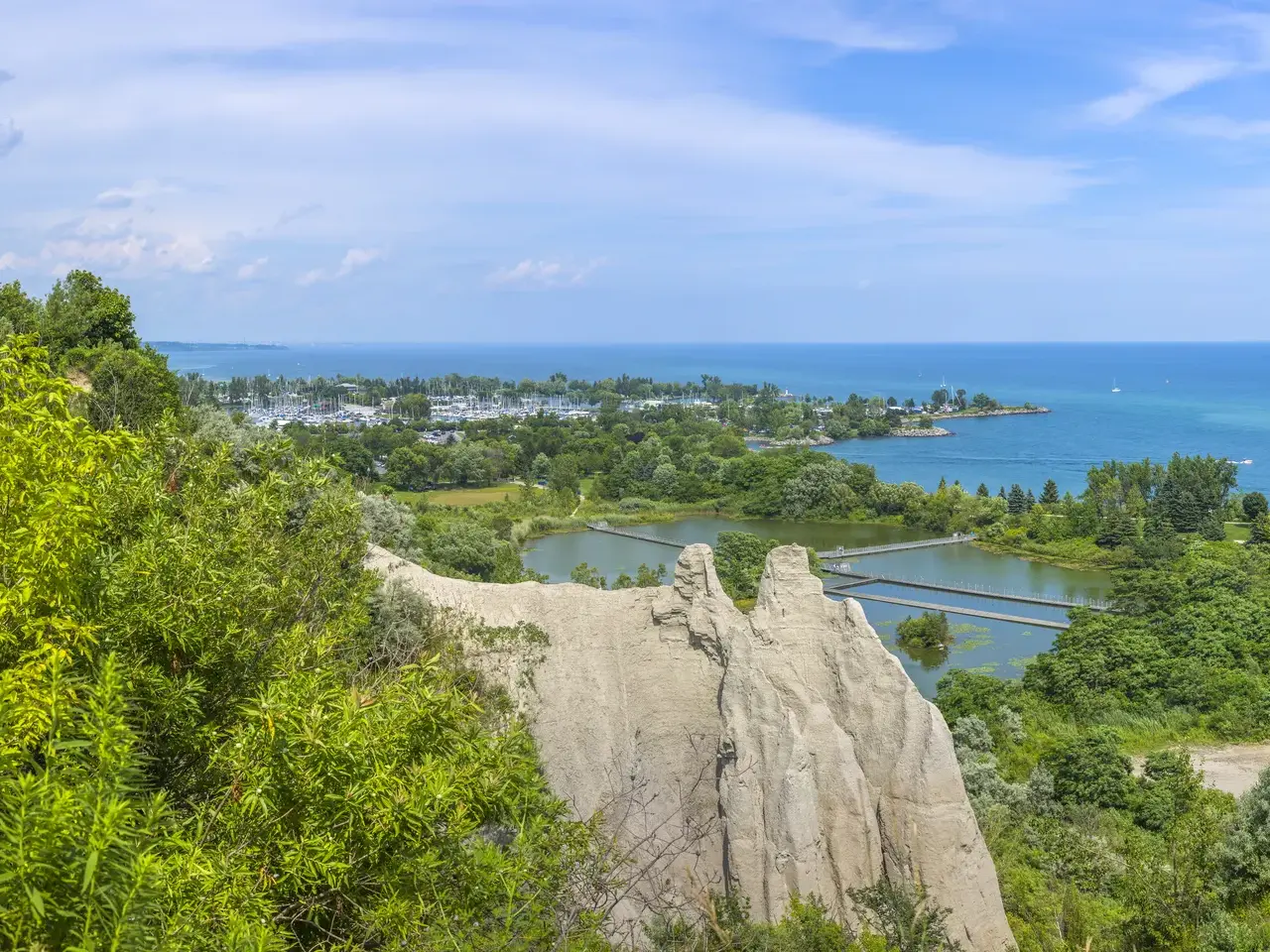 Panoramablick von den Scarborough Cliffs auf den Ontario-See mit einer Marina und grünen Uferlandschaften an einem sonnigen Tag.