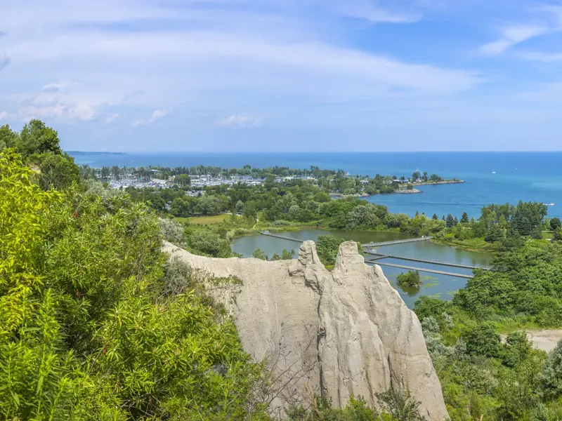 Panoramablick von den Scarborough Cliffs auf den Ontario-See mit einer Marina und grünen Uferlandschaften an einem sonnigen Tag.
