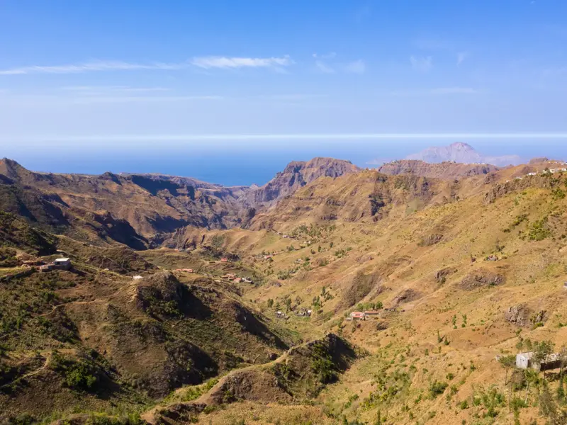 Weitblick über die zerklüftete Berglandschaft von Santiago mit verstreuten Häusern im Tal und dem Atlantik am Horizont.