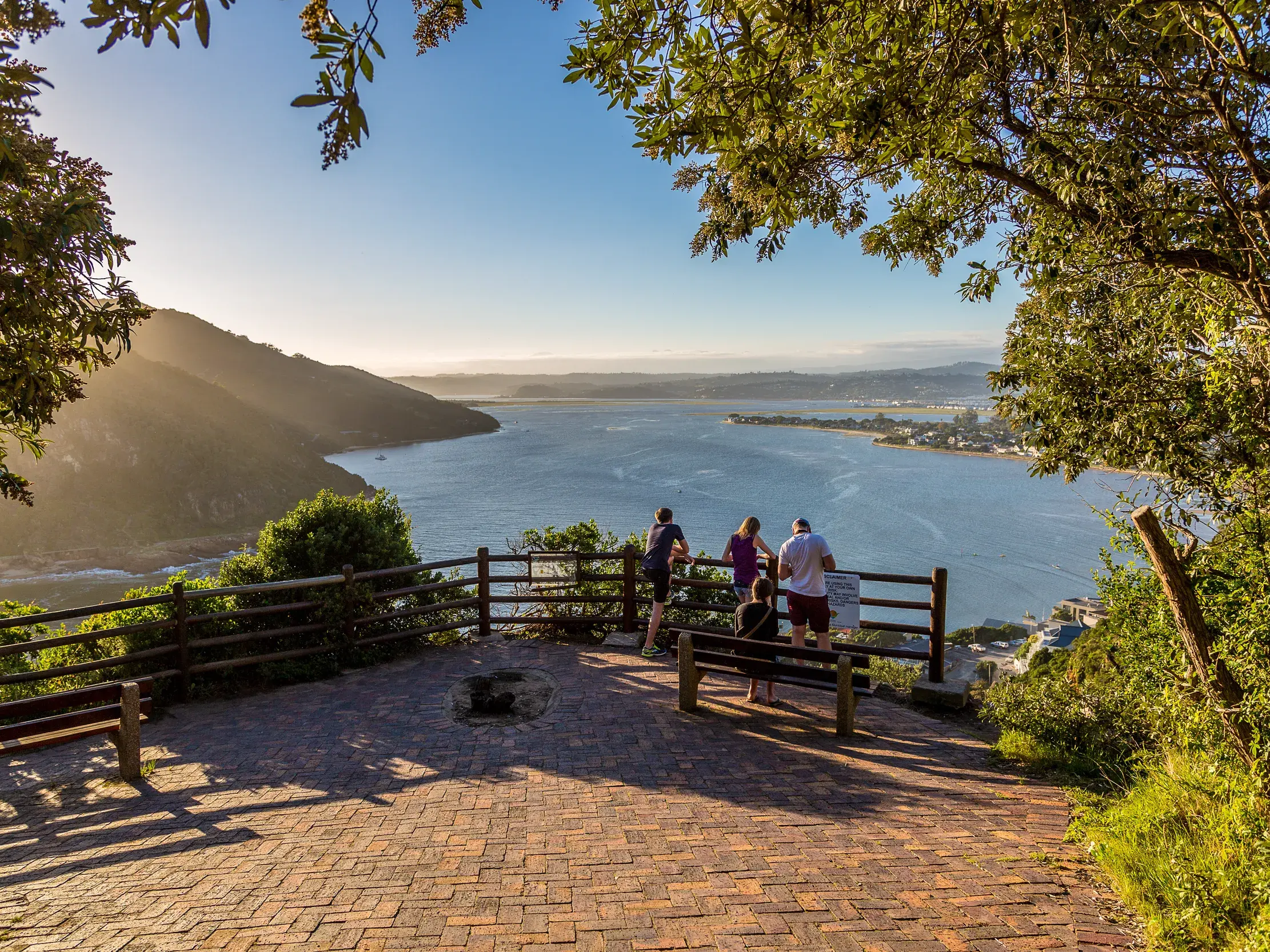 Eine kleine Reisegruppe blickt von einem Aussichtspunkt über die malerische Knysna Lagune an der Garden Route in Südafrika.