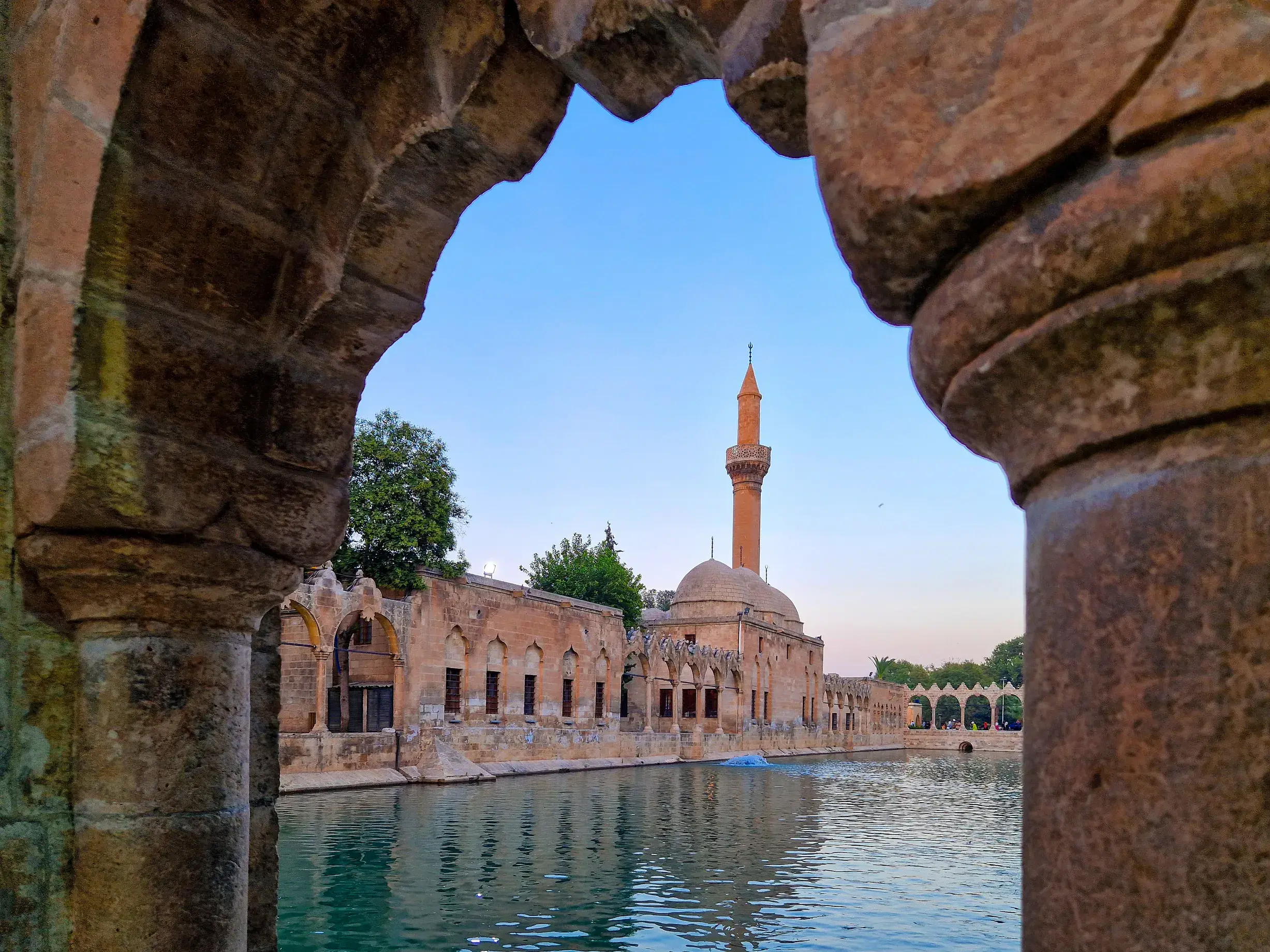 Blick durch einen Steinbogen auf den Fischteich von Abraham und die angrenzende Moschee in der Parkanlage in Sanliurfa.