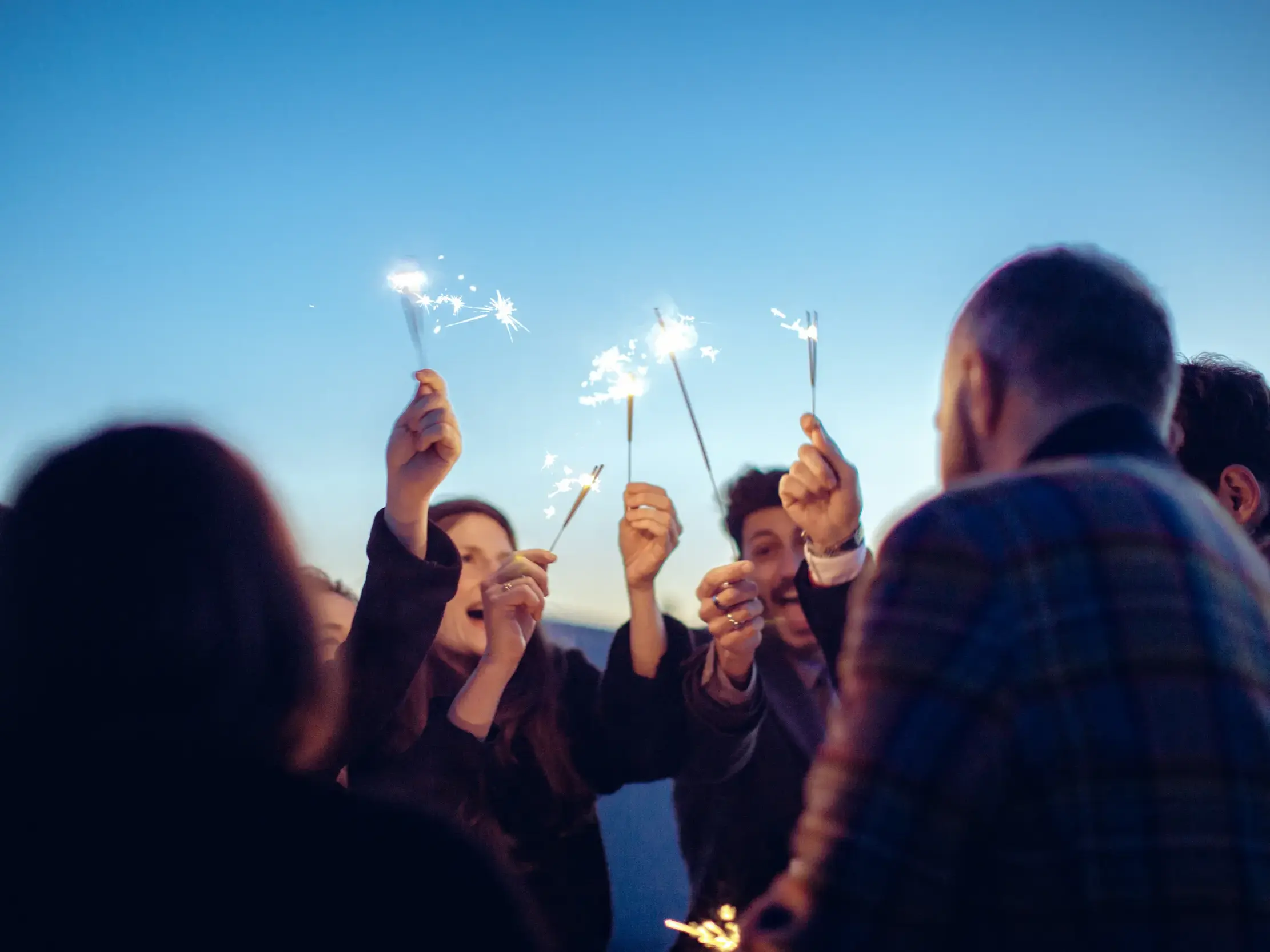 Fröhliche Reisegruppe feiert gemeinsam Silvester in Ljubljana und hält leuchtende Wunderkerzen in den Abendhimmel.