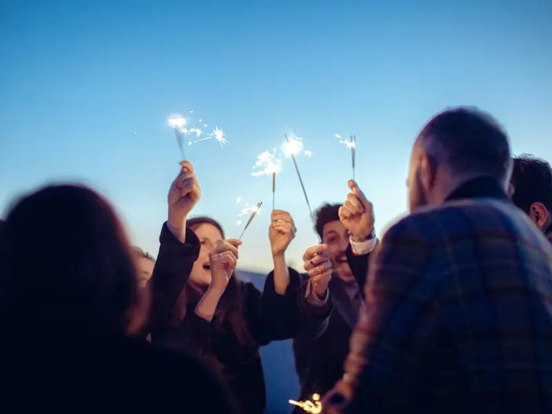 Fröhliche Reisegruppe feiert gemeinsam Silvester in Ljubljana und hält leuchtende Wunderkerzen in den Abendhimmel.