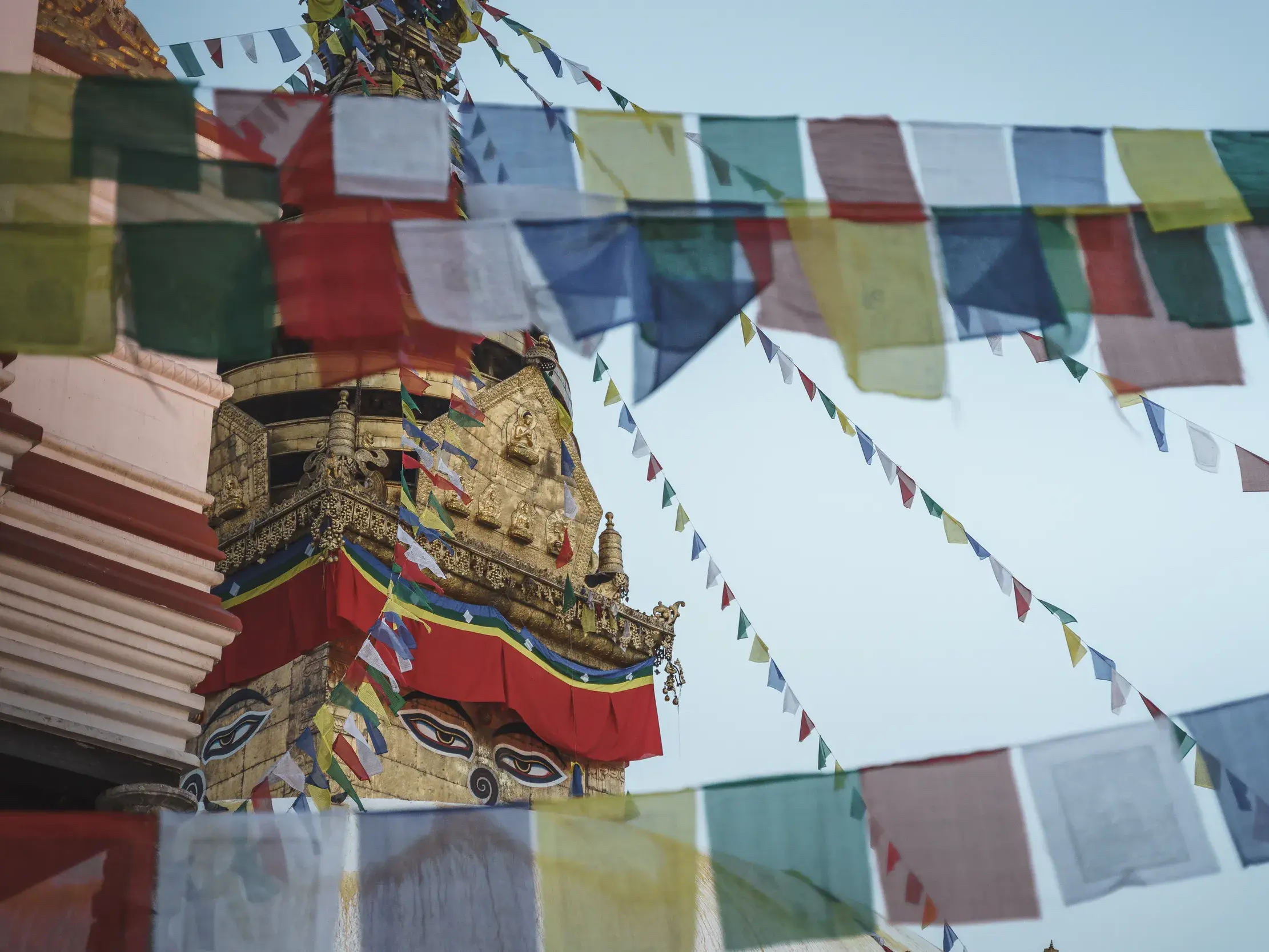 Zahlreiche bunte, buddhistische Gebetsfahnen wehen im Wind vor der goldenen Kuppel des Swayambhunath Stupas in Kathmandu.