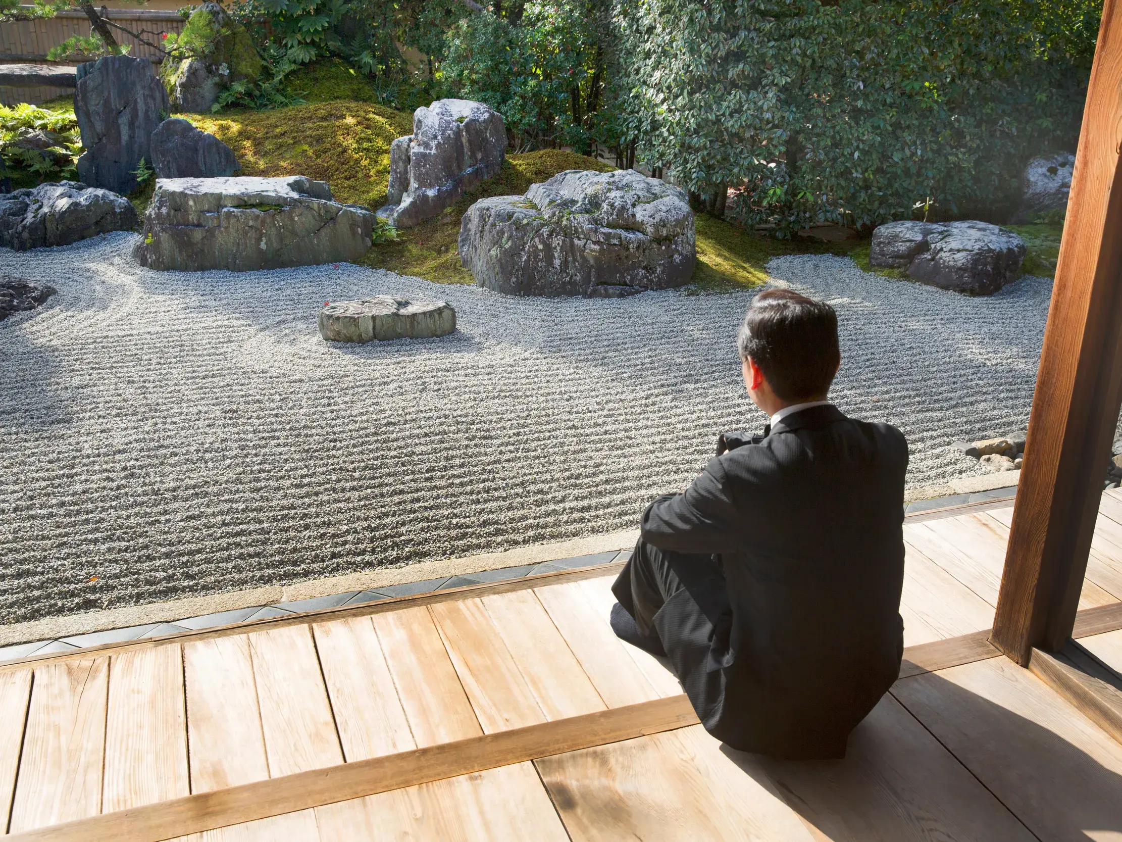 Ein Reisender sitzt auf einer Holzterrasse und betrachtet den berühmten Zen-Garten des Ryoan-Tempels in Kyoto.