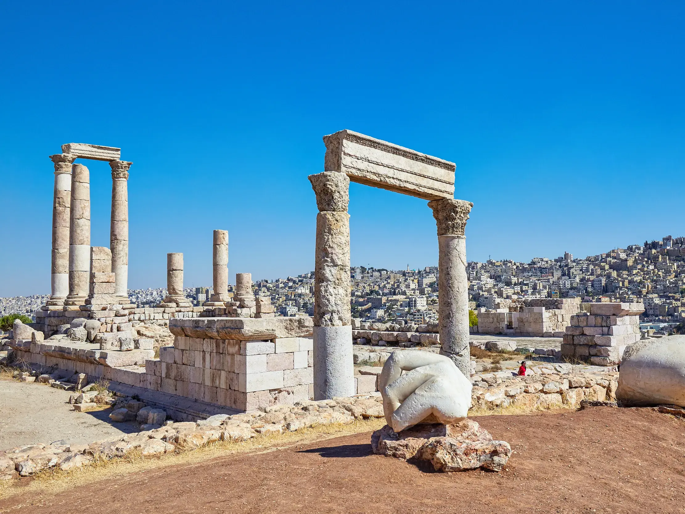 Antike Ruinen des Herkulestempels auf der Zitadelle von Amman mit weitem Panoramablick auf die moderne Stadt bei blauem Himmel.