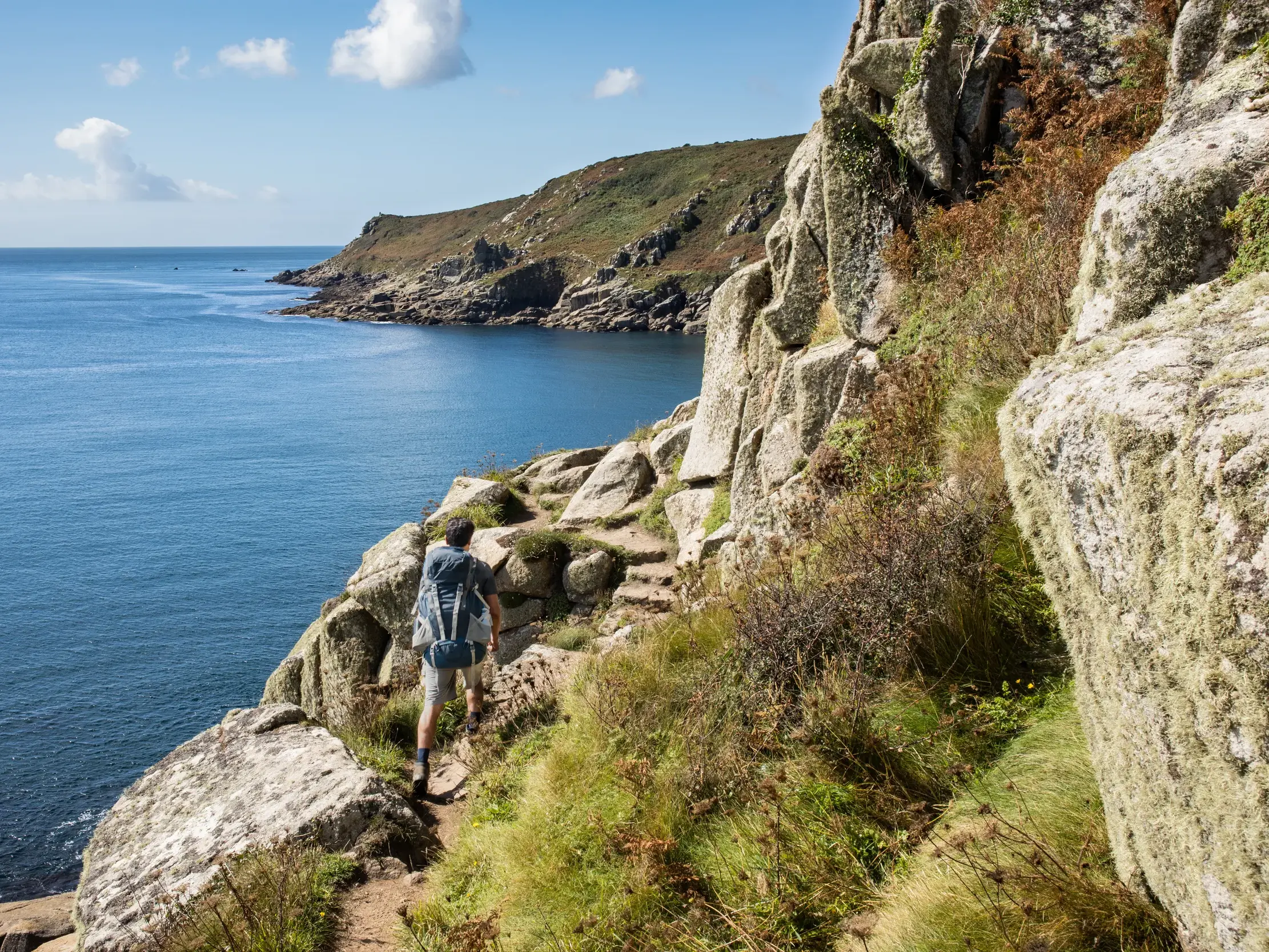 Wanderer mit Rucksack auf dem felsigen Klippenpfad des South West Coast Path mit Blick auf die Küste Cornwalls.