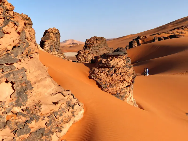 Zwei Wanderer beim Trekking durch die bizarr geformte Dünen- und Felsenlandschaft des Tadrart in der algerischen Sahara.