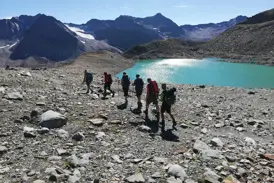 Eine kleine Wandergruppe wandert auf einem steinigen Weg an einem türkisen Gletschersee in den Stubaier Alpen vorbei.