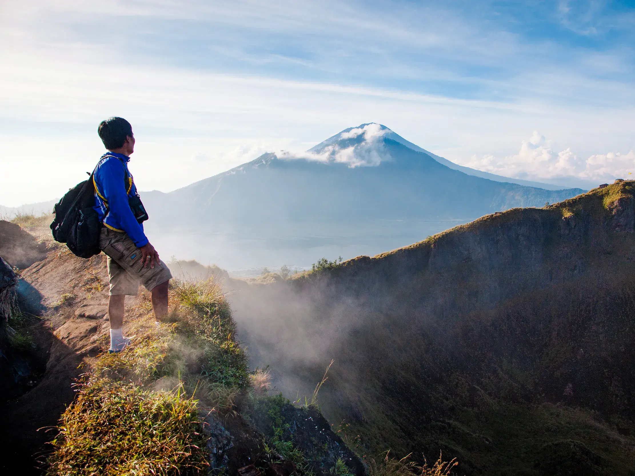 Wanderer mit Rucksack steht am Kraterrand des Mt. Bromo in Java und blickt bei Sonnenaufgang auf die Vulkanlandschaft.