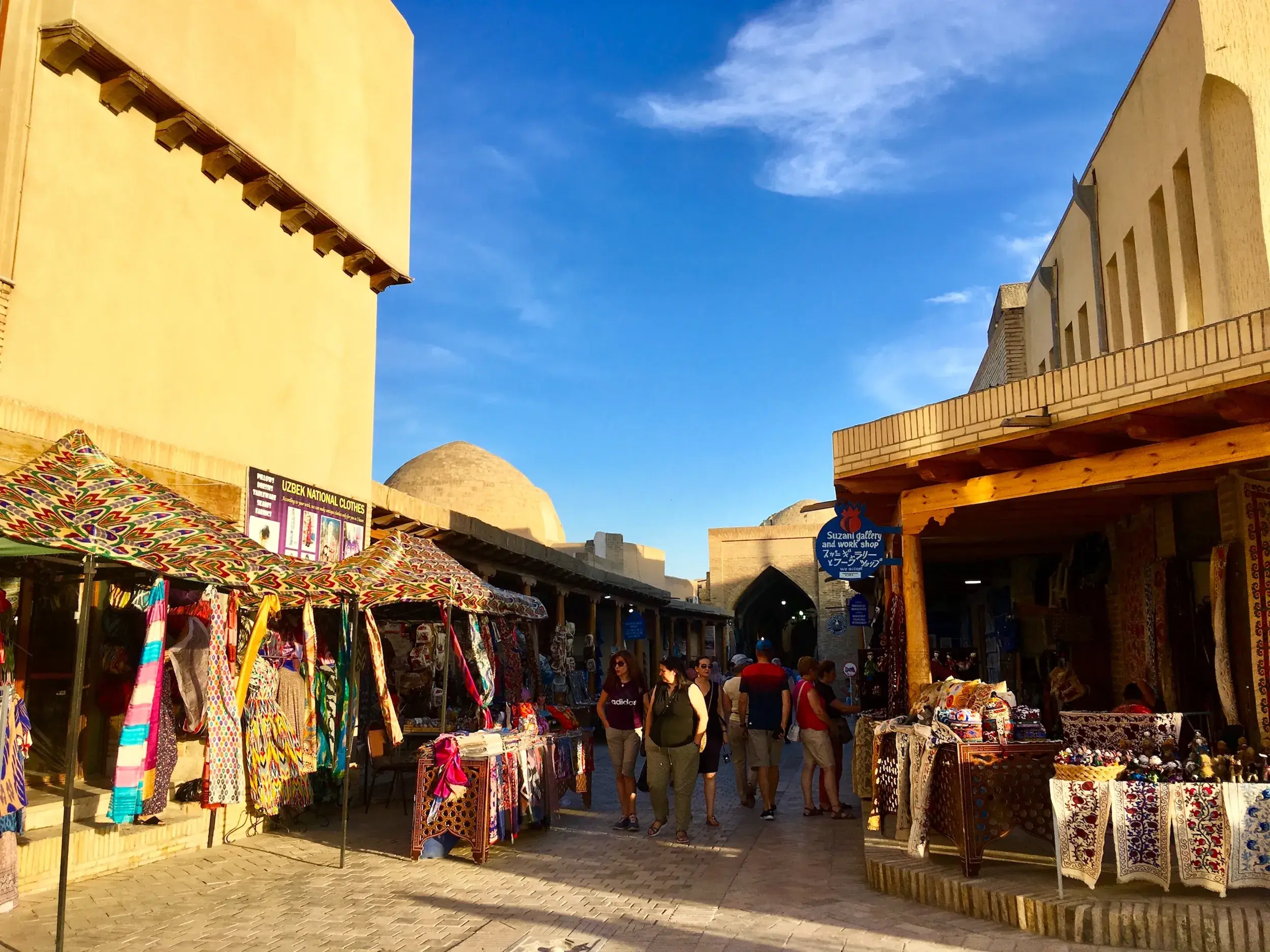 Eine Reisegruppe erkundet einen lebhaften Basar mit bunten Textilien in den historischen Gassen von Buchara, Usbekistan.