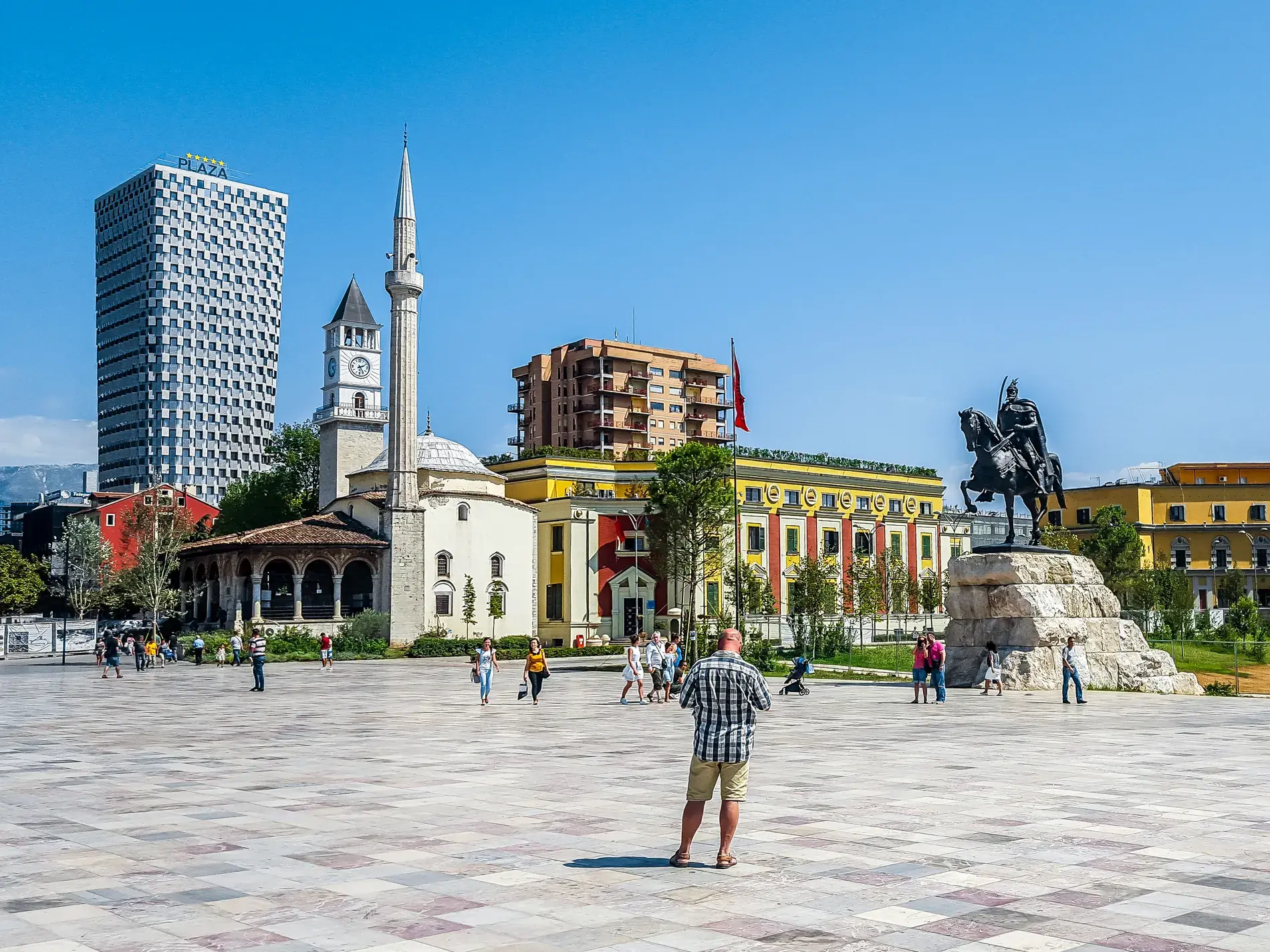 Der sonnige Skanderbeg-Platz in Tirana mit der Et'hem-Bey-Moschee, der Reiterstatue und moderner Architektur im Hintergrund.