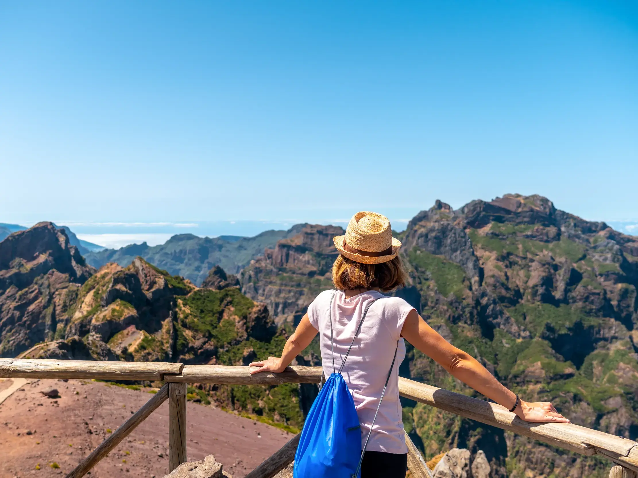 Eine Frau mit Strohhut genießt am Pico do Arieiro den Panoramablick auf die schroffe, grüne Berglandschaft Madeiras.