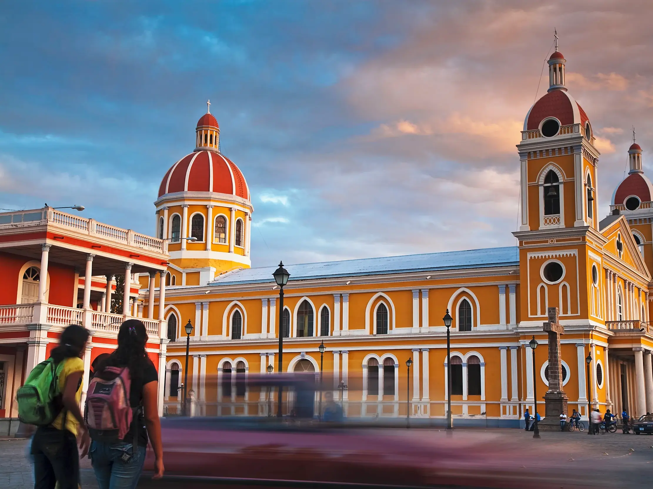 Zwei Frauen auf einer Studienreise betrachten die imposante gelbe Kathedrale von Granada in Nicaragua bei Sonnenuntergang.
