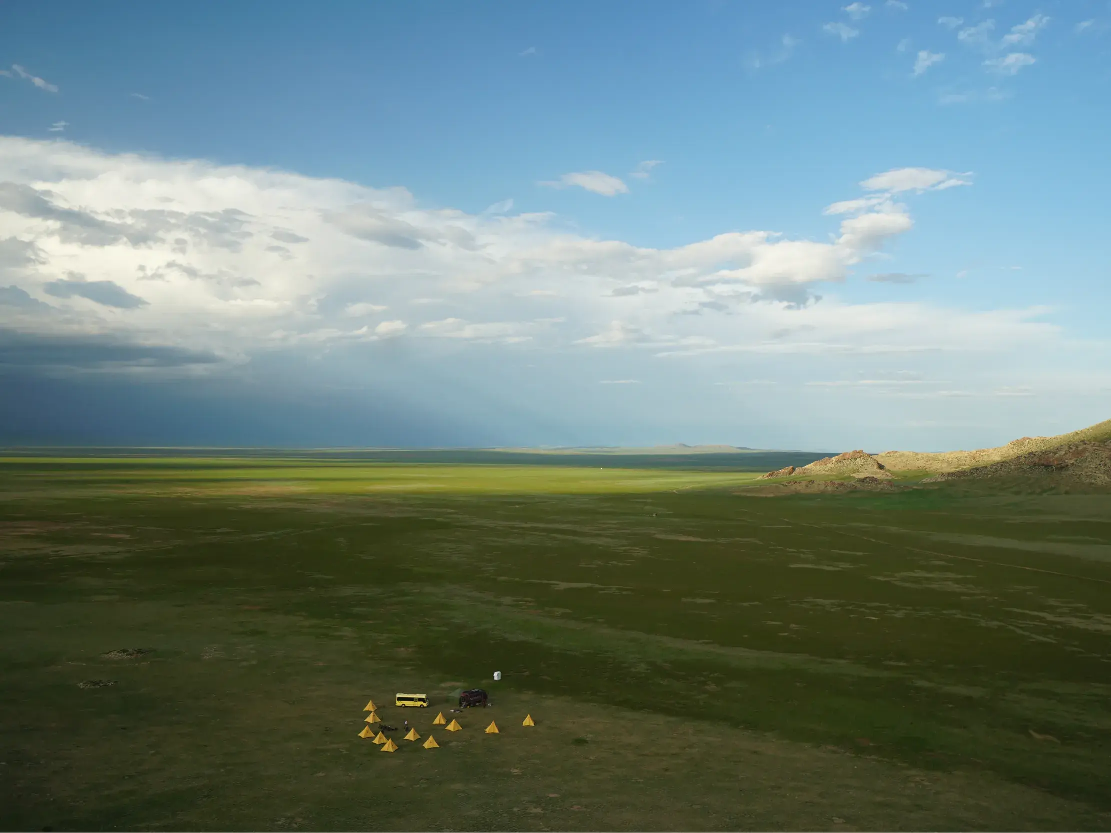 Kleines Zeltlager mit gelben Zelten in der endlosen, grünen Steppe der Mongolei während einer Hauser Trekkingreise.