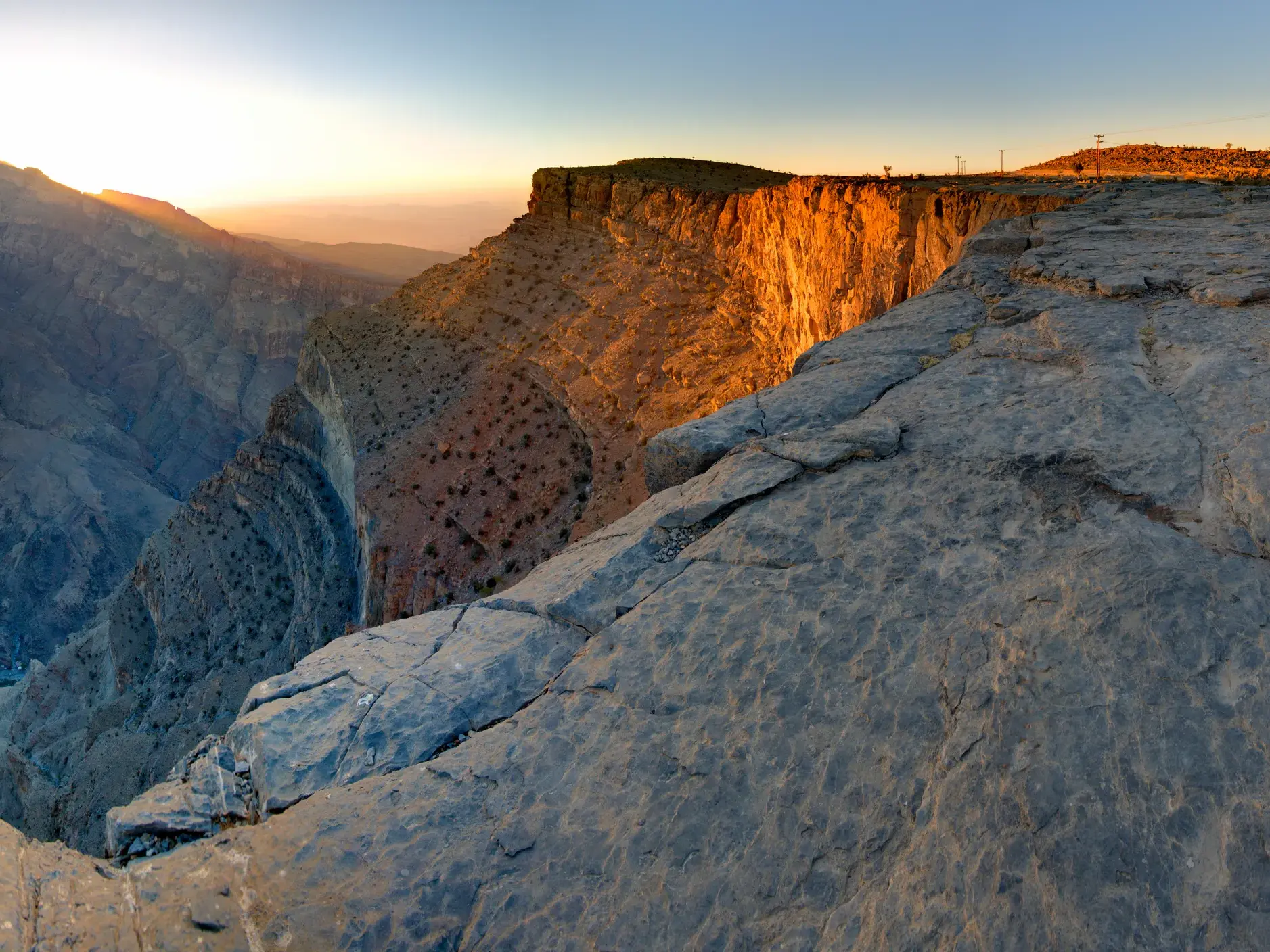 Die untergehende Sonne taucht die Felswände des Dschebel Schems, dem Grand Canyon Omans, in ein warmes, goldenes Licht.