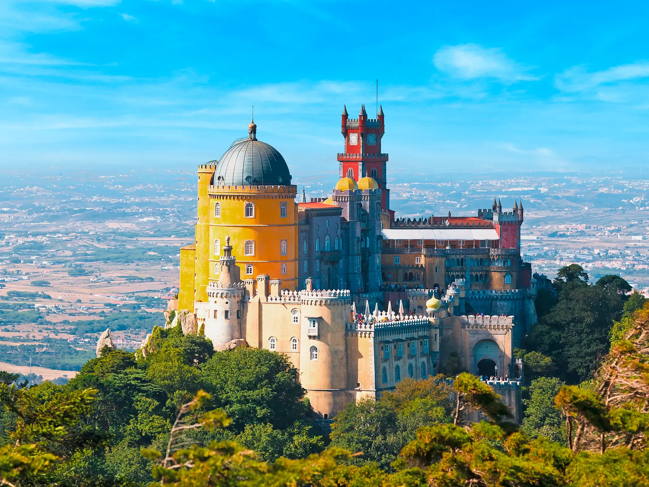 Farbenprächtiger Palast des UNESCO-Welterbes Sintra, der auf einem bewaldeten Hügel über die Landschaft Portugals blickt.