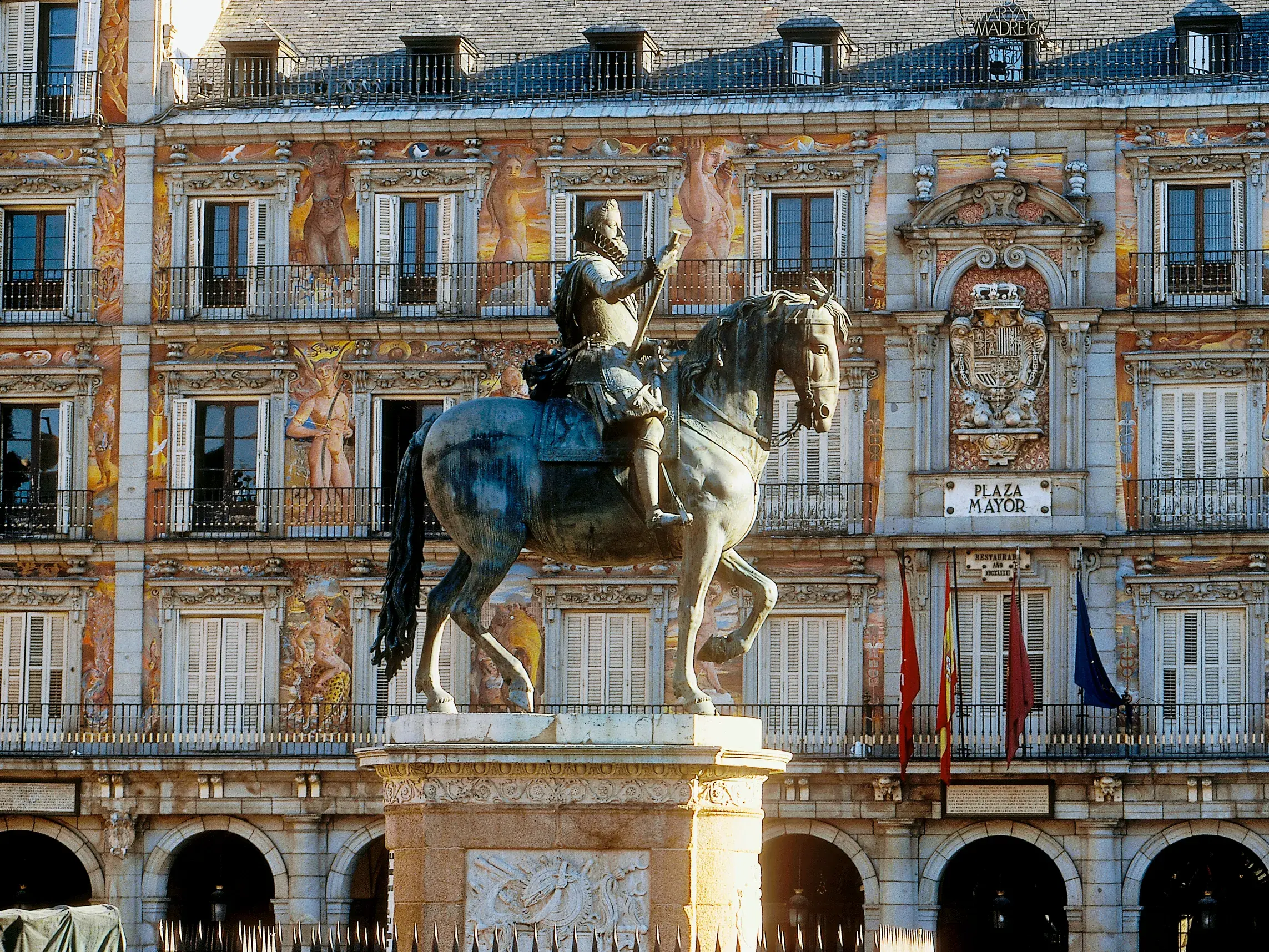 Bronzenes Reiterstandbild im Zentrum der Plaza Mayor in Madrid vor der prunkvoll bemalten Fassade eines historischen Gebäudes.
