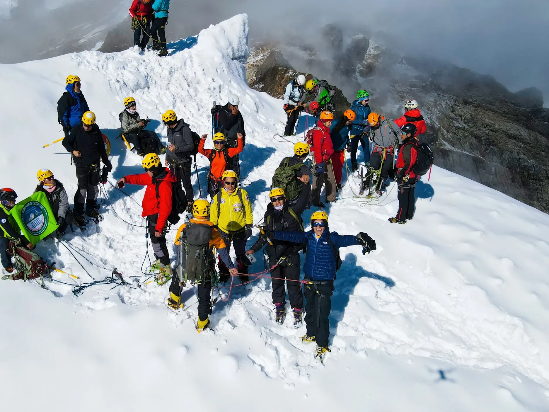 Eine Bergsteiger-Gruppe mit Bergführern feiert den Gipfelerfolg auf einem schneebedeckten Gipfel der Cordillera Blanca in Peru.