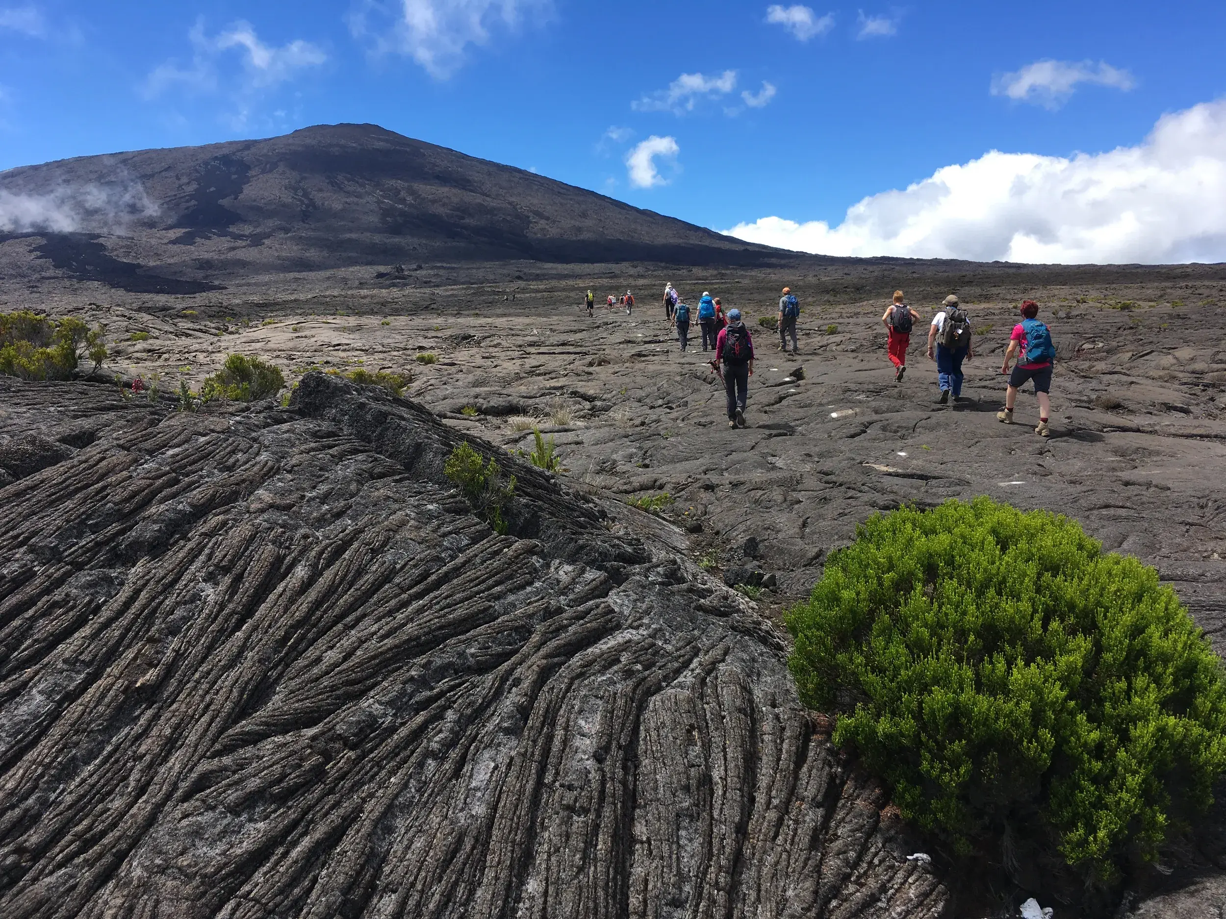 Eine Reisegruppe wandert auf einem Pfad über weite, erstarrte Lavafelder zum Krater des Vulkans Piton de la Fournaise.