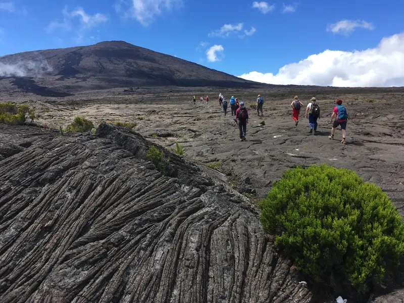 Eine Reisegruppe wandert auf einem Pfad über weite, erstarrte Lavafelder zum Krater des Vulkans Piton de la Fournaise.