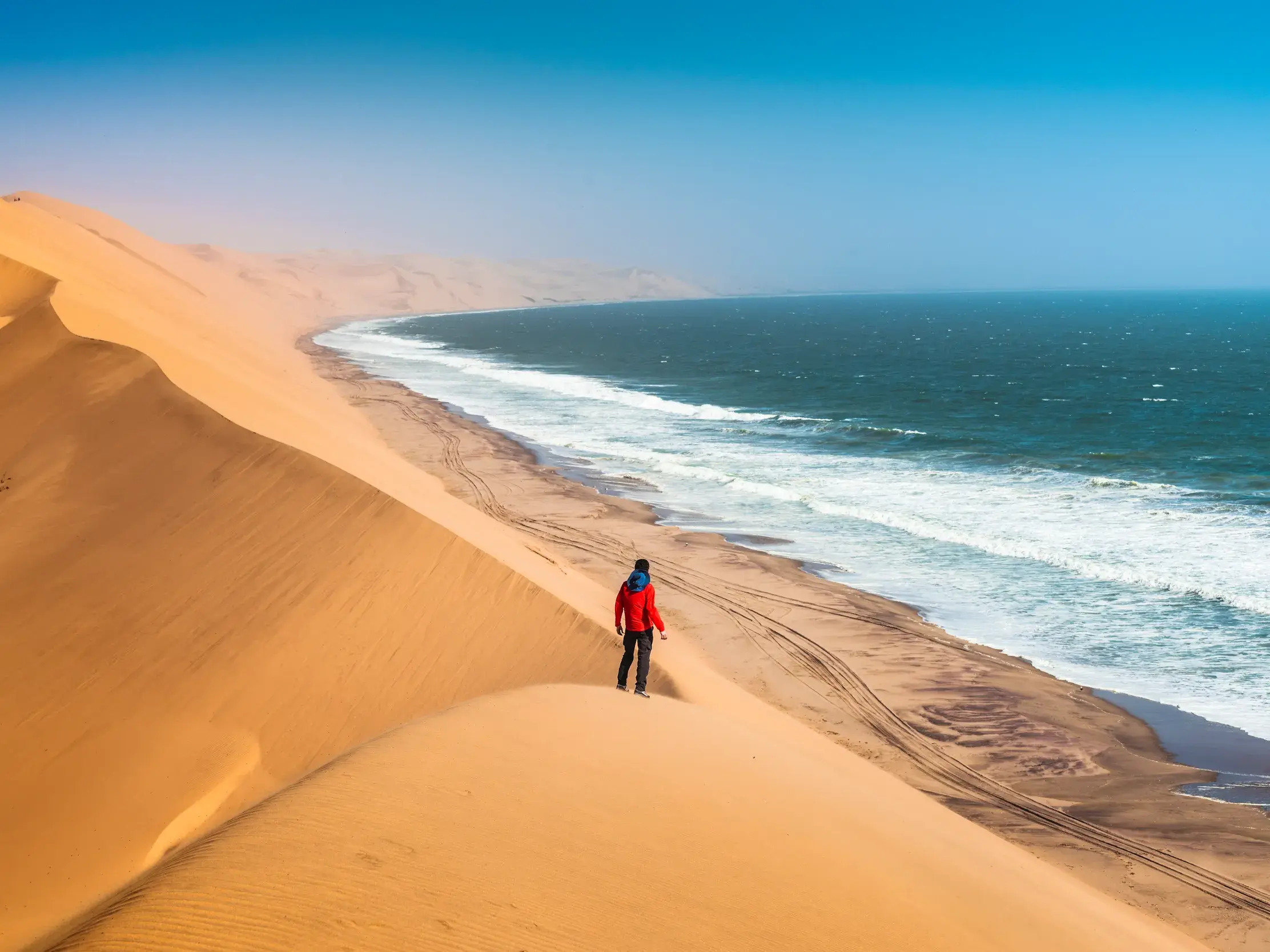 Ein Reiseteilnehmer blickt von einer hohen Sanddüne auf die Küste Namibias, wo die Namib-Wüste den Atlantik berührt.
