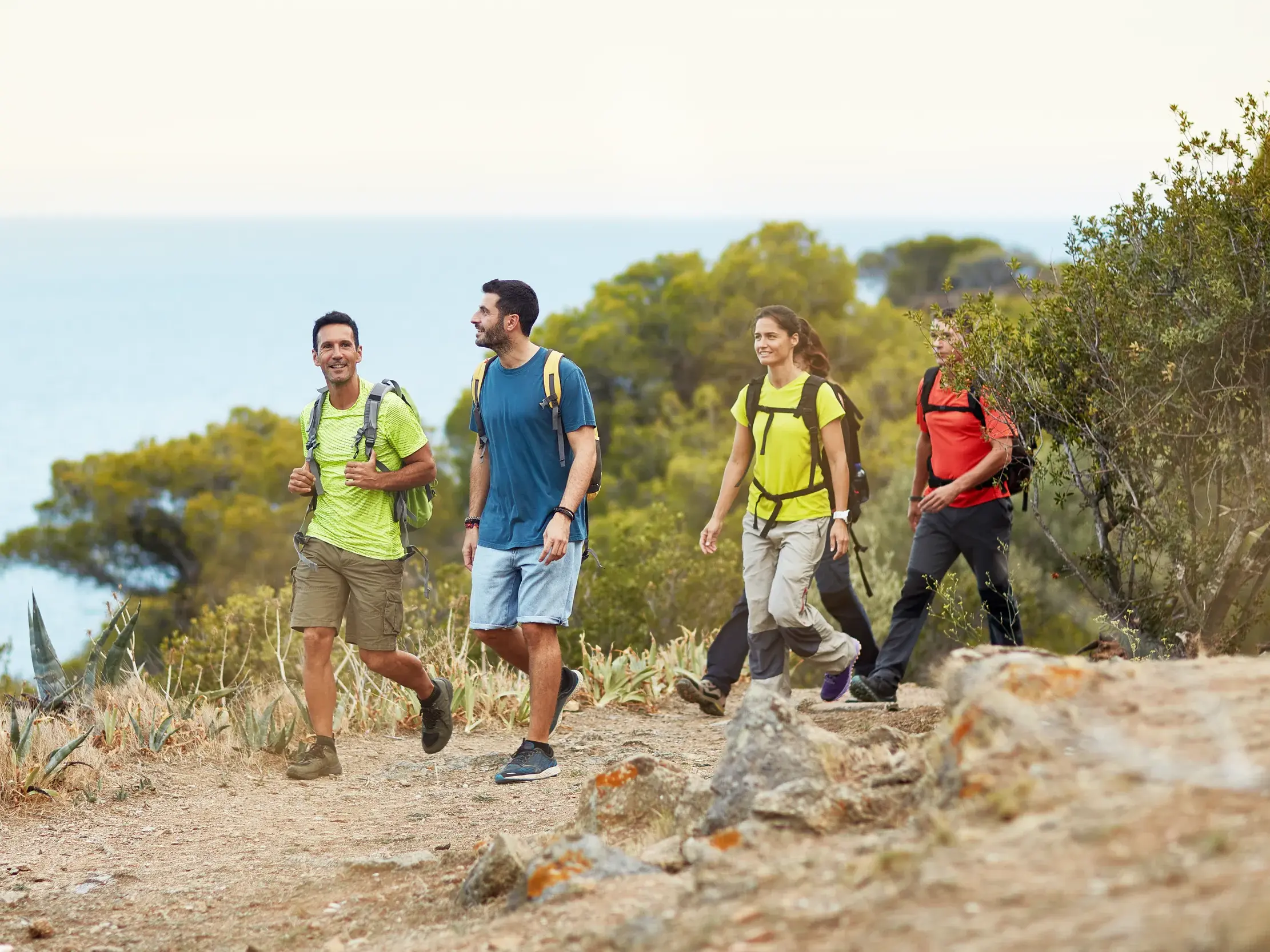 Eine kleine Reisegruppe wandert auf einem sonnigen Küstenpfad in Griechenland mit weitem Blick über das Meer bei Kap Araxos.