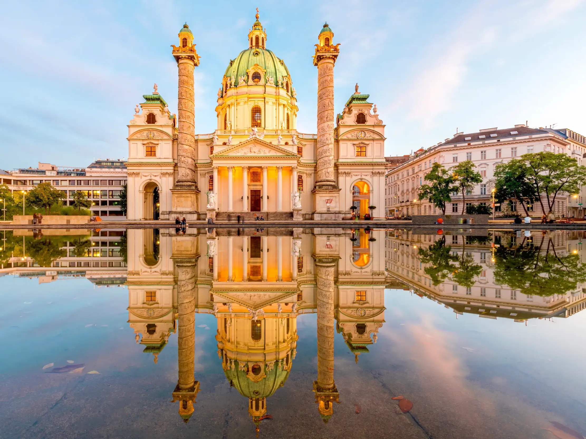 Die prachtvolle barocke Karlskirche in Wien bei Dämmerung, deren Fassade sich symmetrisch im Wasser davor spiegelt.