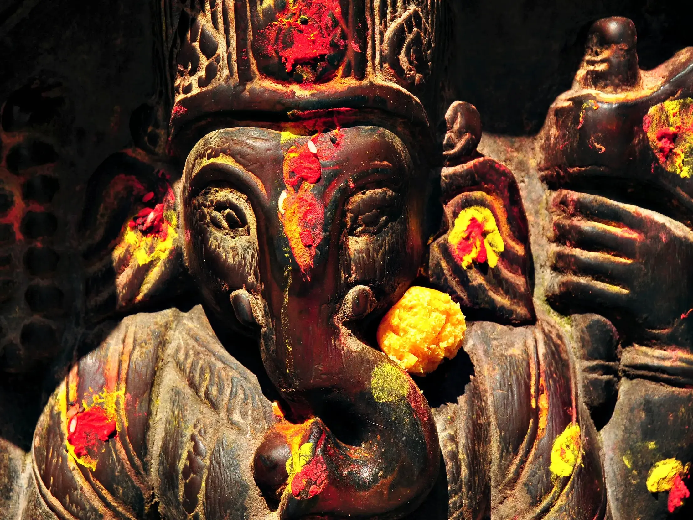 Nahaufnahme einer kunstvoll geschnitzten Ganesha-Statue in Kathmandu, mit rotem Farbpulver und einer gelben Opfergabe.