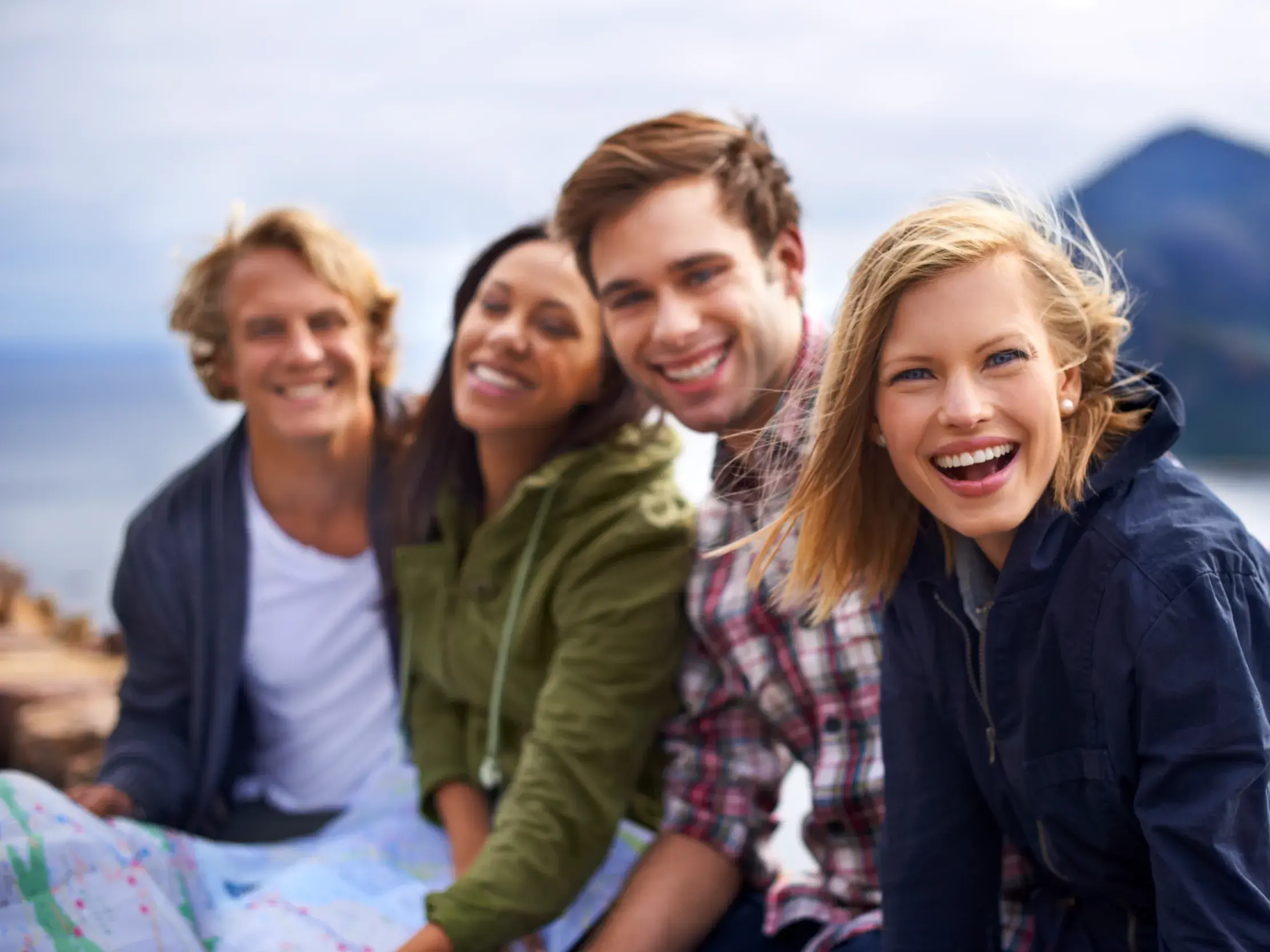 Vier glückliche junge Leute auf einer Gruppenreise in Norwegen, die lachend vor einer Fjordlandschaft posieren.
