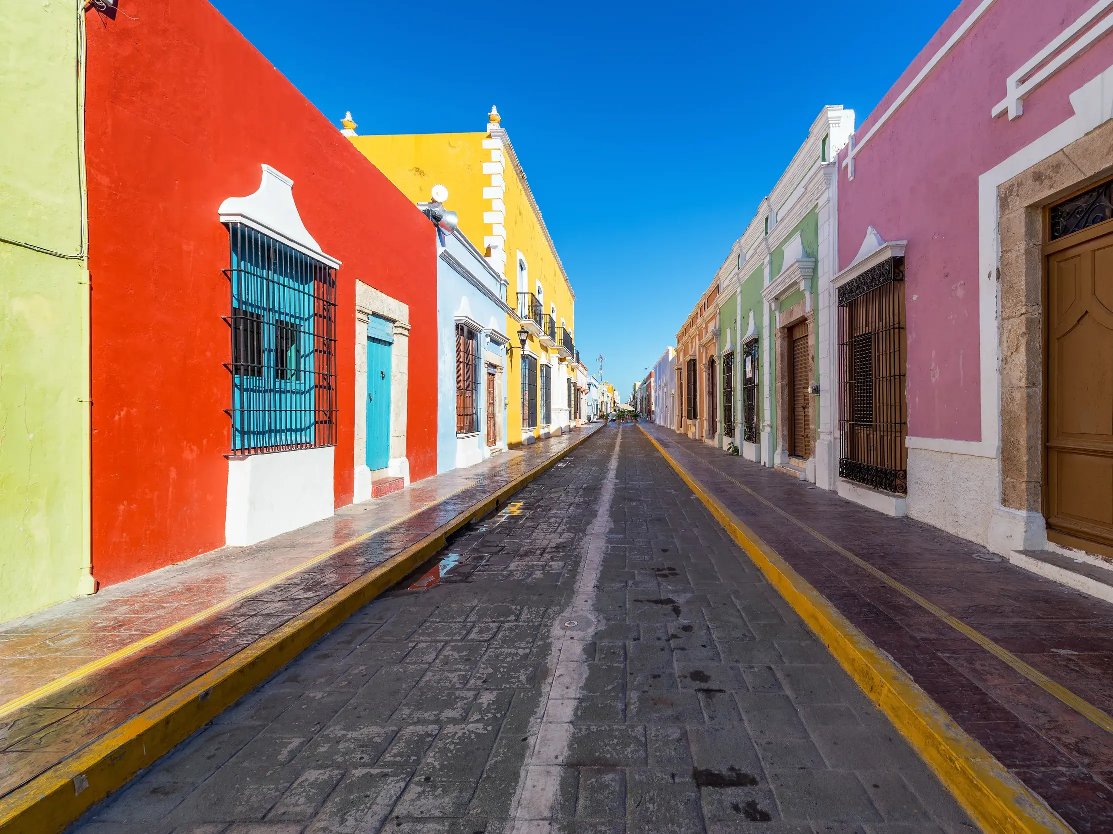 Leuchtend bunte Fassaden von Kolonialhäusern säumen eine leere Kopfsteinpflasterstraße in der Altstadt von Campeche.