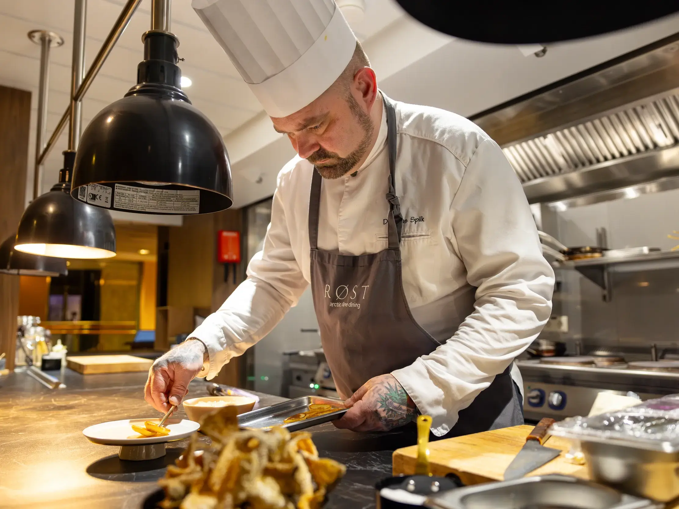 Ein Koch der Hurtigruten richtet in der Bordküche konzentriert ein Gericht der Norwegian Coastal Kitchen an.