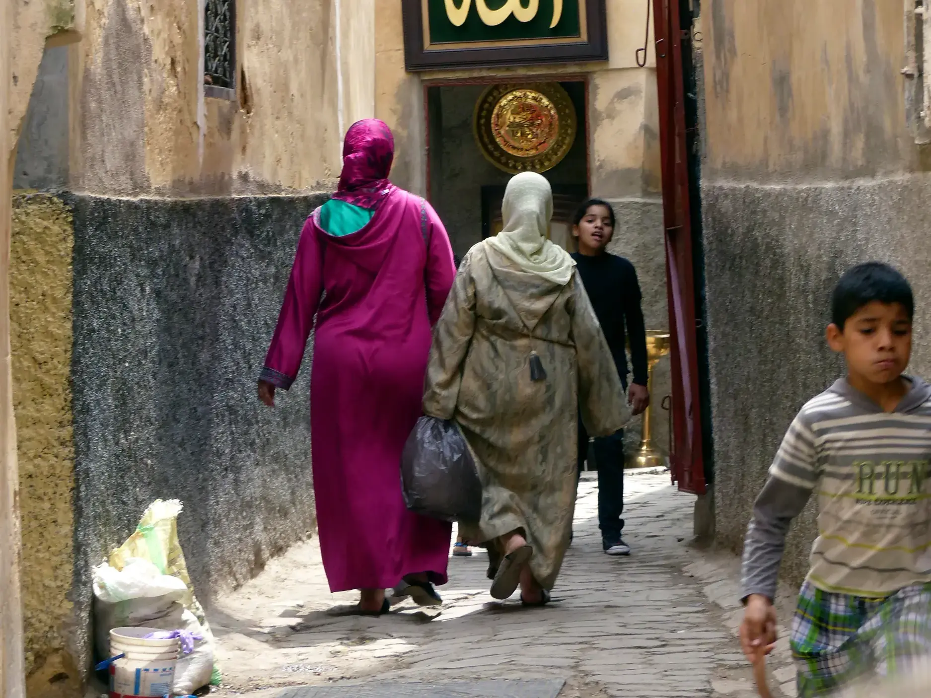 Authentische Begegnung in Marokko: Frauen in Djellabas und Kinder in einer verwinkelten Gasse einer Medina auf einer Wanderreise.