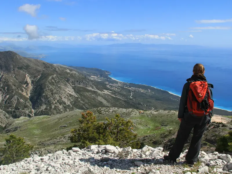Wanderin mit rotem Rucksack auf einem Gipfel im Llogara Nationalpark mit Panoramablick auf die albanische Küste.