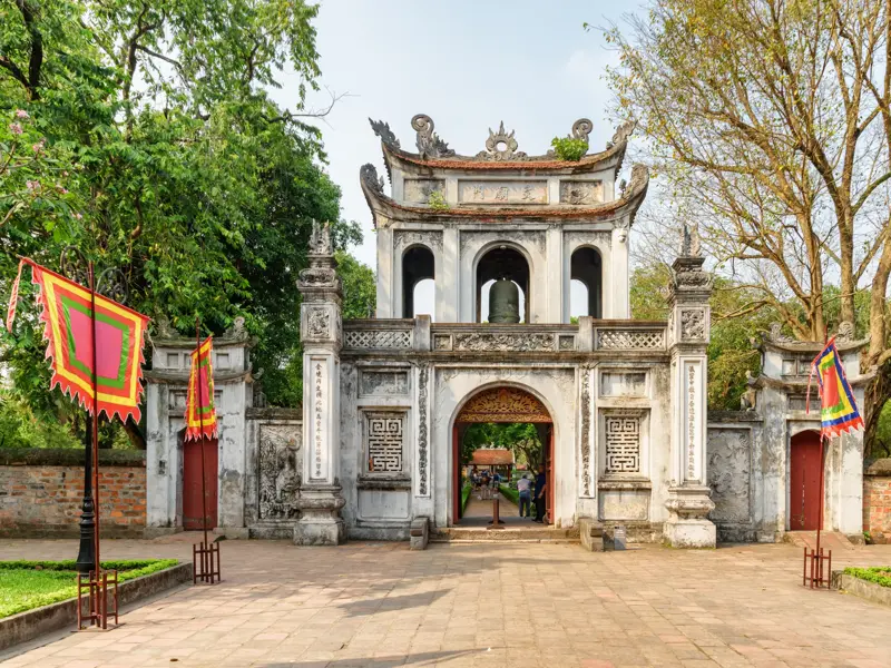 Das historische Eingangstor zum berühmten Literaturtempel in Hanoi, flankiert von bunten Flaggen unter grünen Bäumen.
