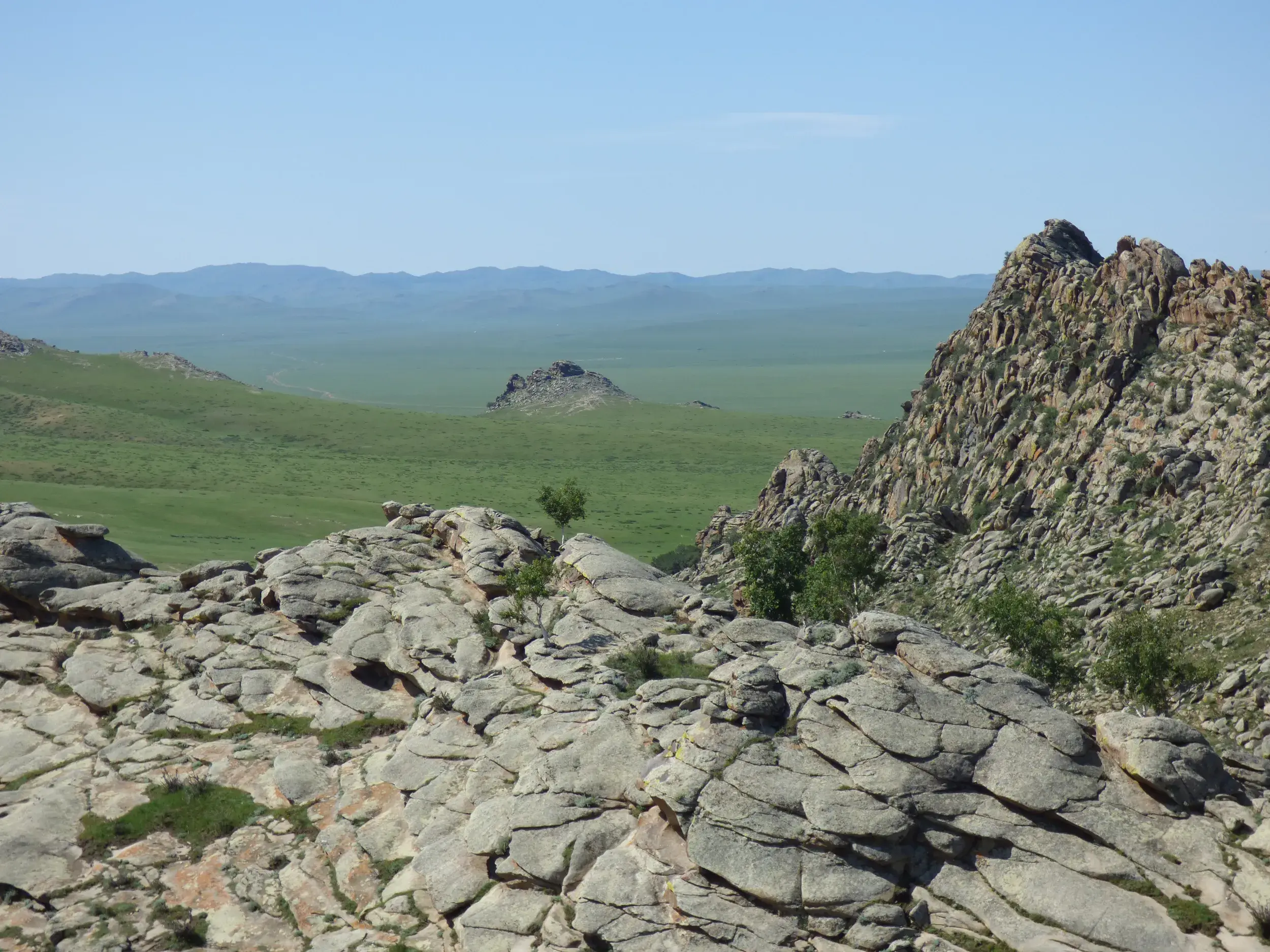 Aussicht von einer felsigen Anhöhe auf die endlose, grüne Steppenlandschaft während des Trekkings im Khan Khentii-Nationalpark.