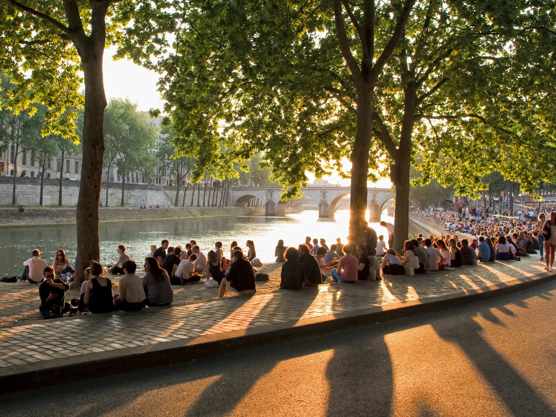 Zahlreiche Menschen entspannen am Ufer der Seine in Paris und genießen das warme, goldene Licht des Sonnenuntergangs.