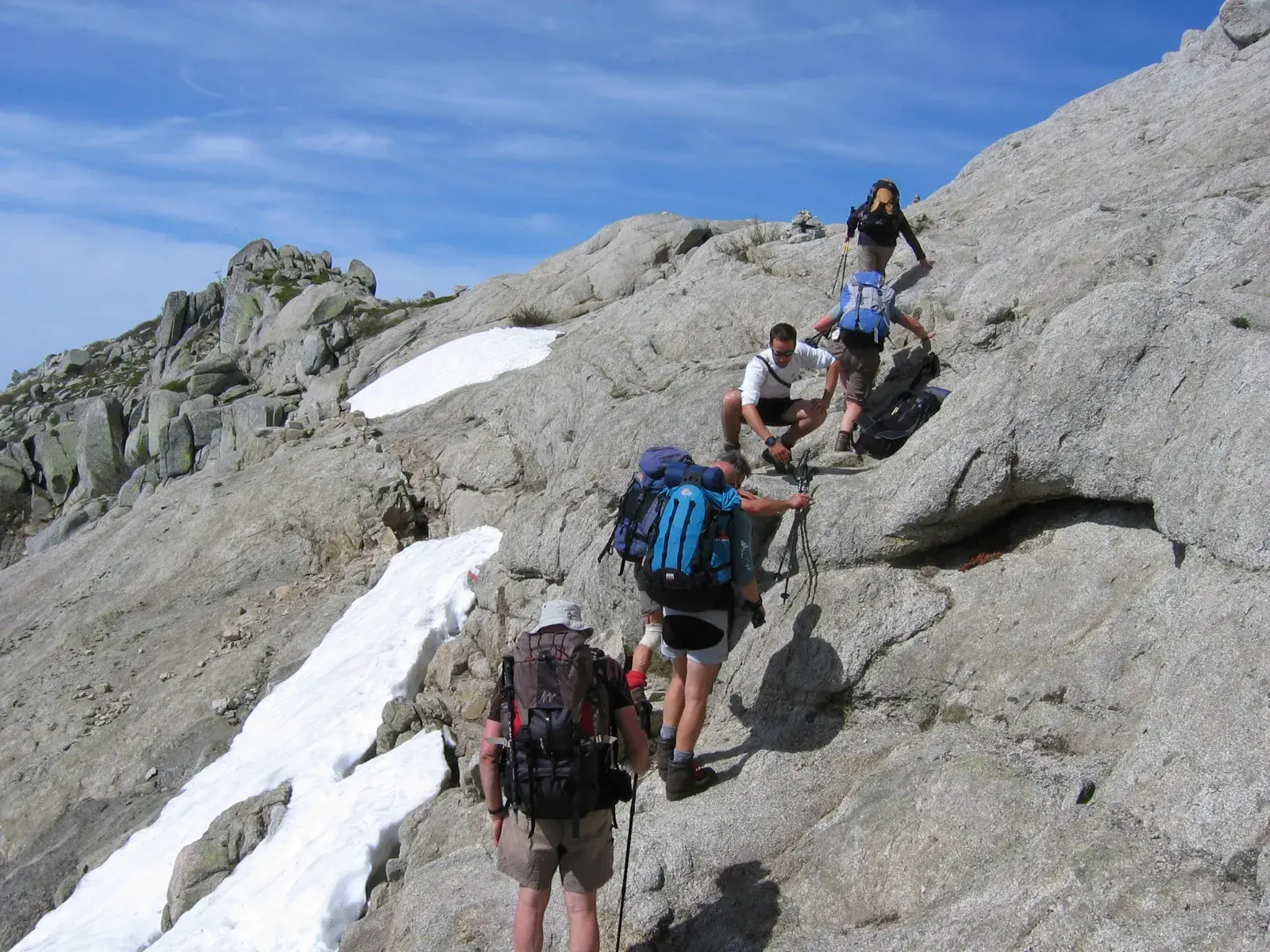 Eine Gruppe von Trekkern überwindet eine steile Felswand mit Schneefeldern auf dem GR20-Fernwanderweg auf Korsika.