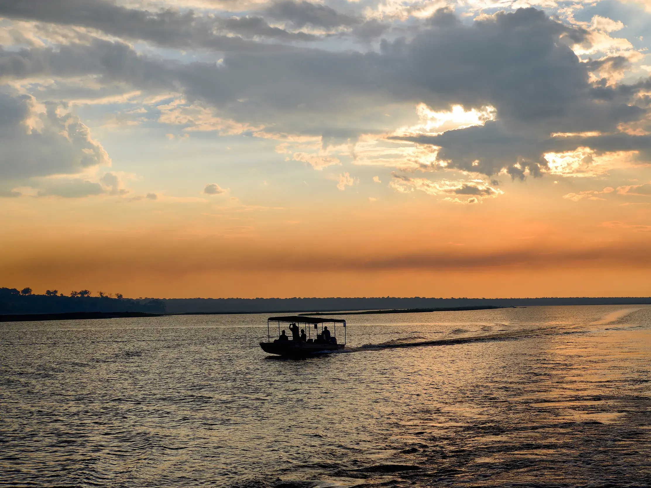 Eine kleine Reisegruppe auf einer Bootssafari auf dem Chobe-Fluss bei stimmungsvollem Sonnenuntergang in Botswana.