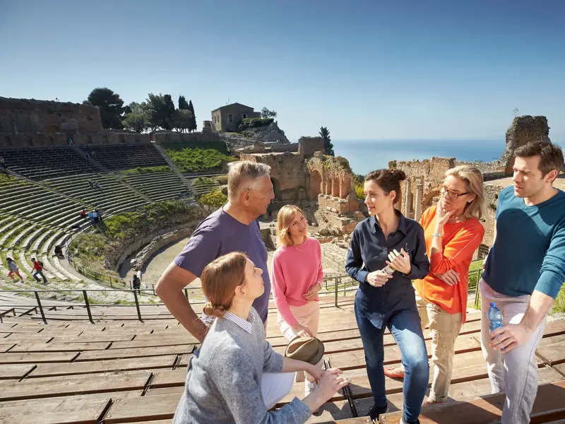 Studiosus-Reiseleiterin erklärt einer Singlereise-Gruppe das antike Theater von Taormina mit fantastischem Blick aufs Meer.