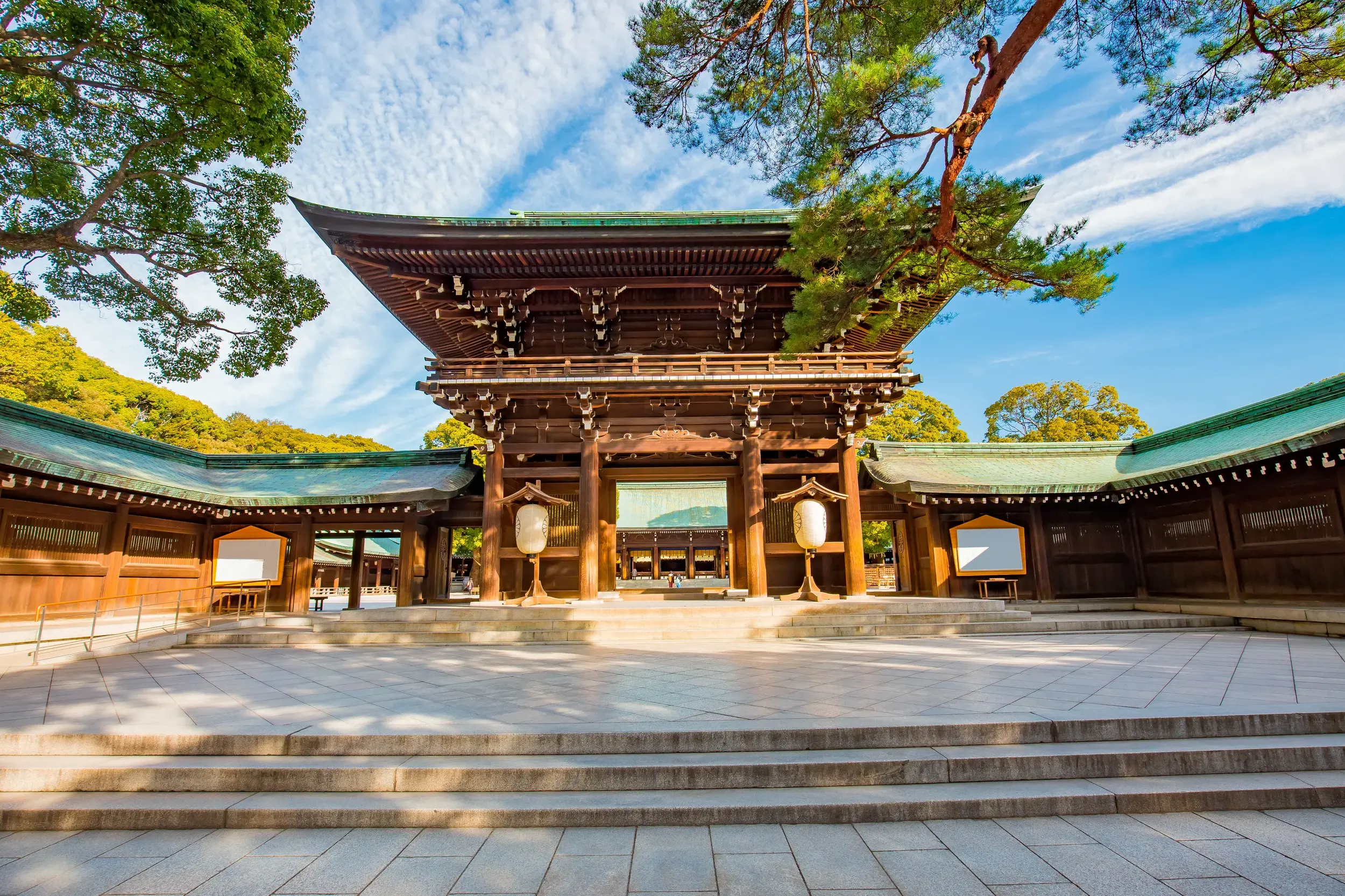 Gepflasterter Vorhof des stillen Meiji-Schreins in Tokio mit Blick auf das traditionelle, hölzerne Haupttor bei Sonnenschein.